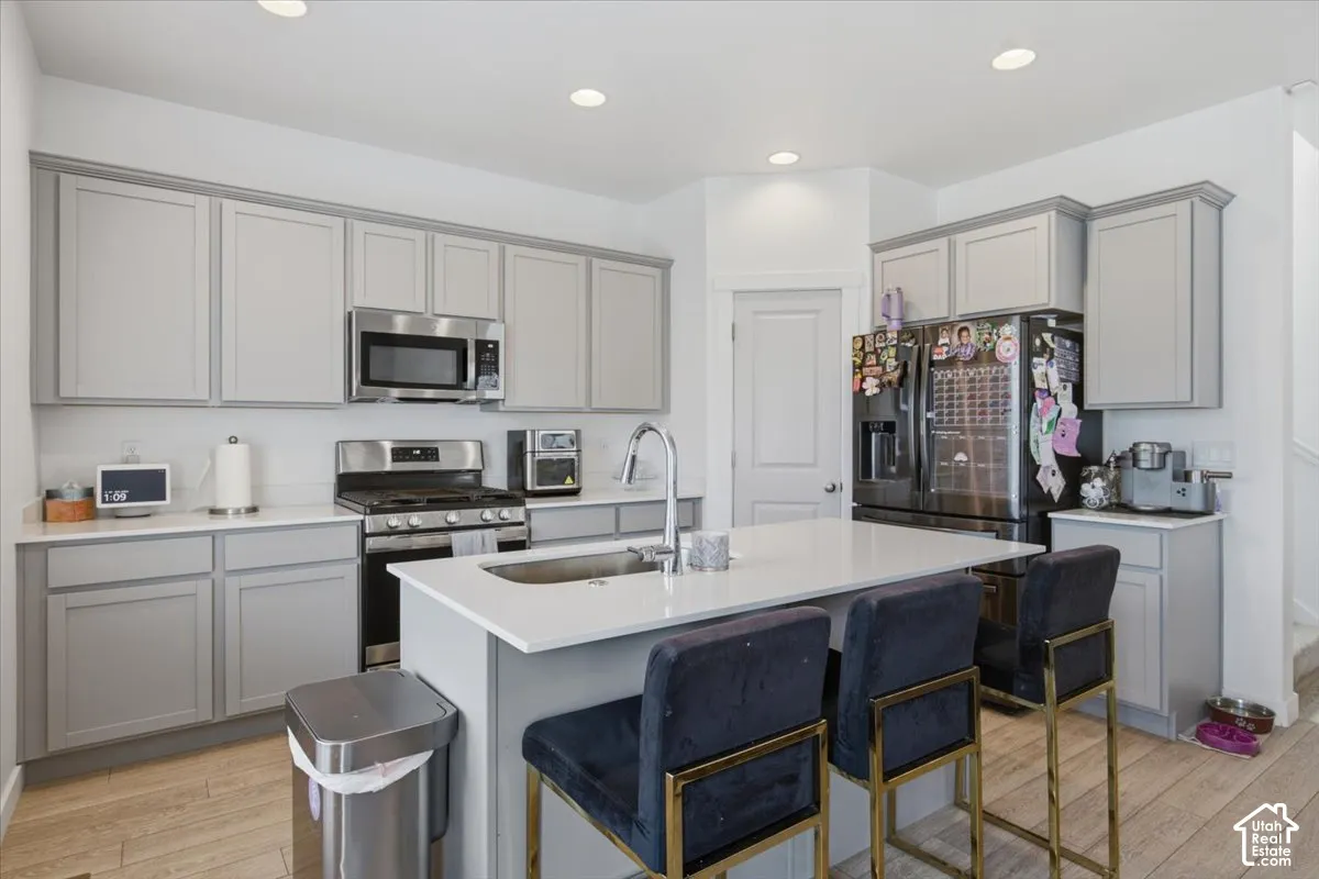 Kitchen featuring light gray shaker-style cabinetry, a central island with a solid-surface countertop, stainless steel appliances, and wood-finish flooring