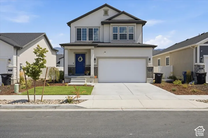 Two-story stucco and brick exterior featuring a covered front porch, an attached two-car garage, concrete driveway, and front landscaping