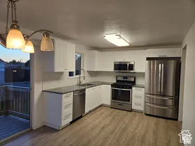 Kitchen featuring white cabinetry, stone-surface countertops, stainless steel appliances, and wood-finish flooring