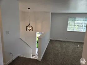Interior space featuring neutral wall tones, wall-to-wall carpeting, a window with horizontal blinds, and a suspended geometric-frame pendant light fixture