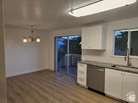 Kitchen and dining area featuring white shaker-style cabinetry, high-contrast stone countertops, wood-finish flooring, a stainless steel dishwasher, and sliding glass doors