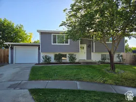 Split-level exterior featuring horizontal lap siding, white brick lower facade, attached one-car garage, concrete driveway, and mature landscaping