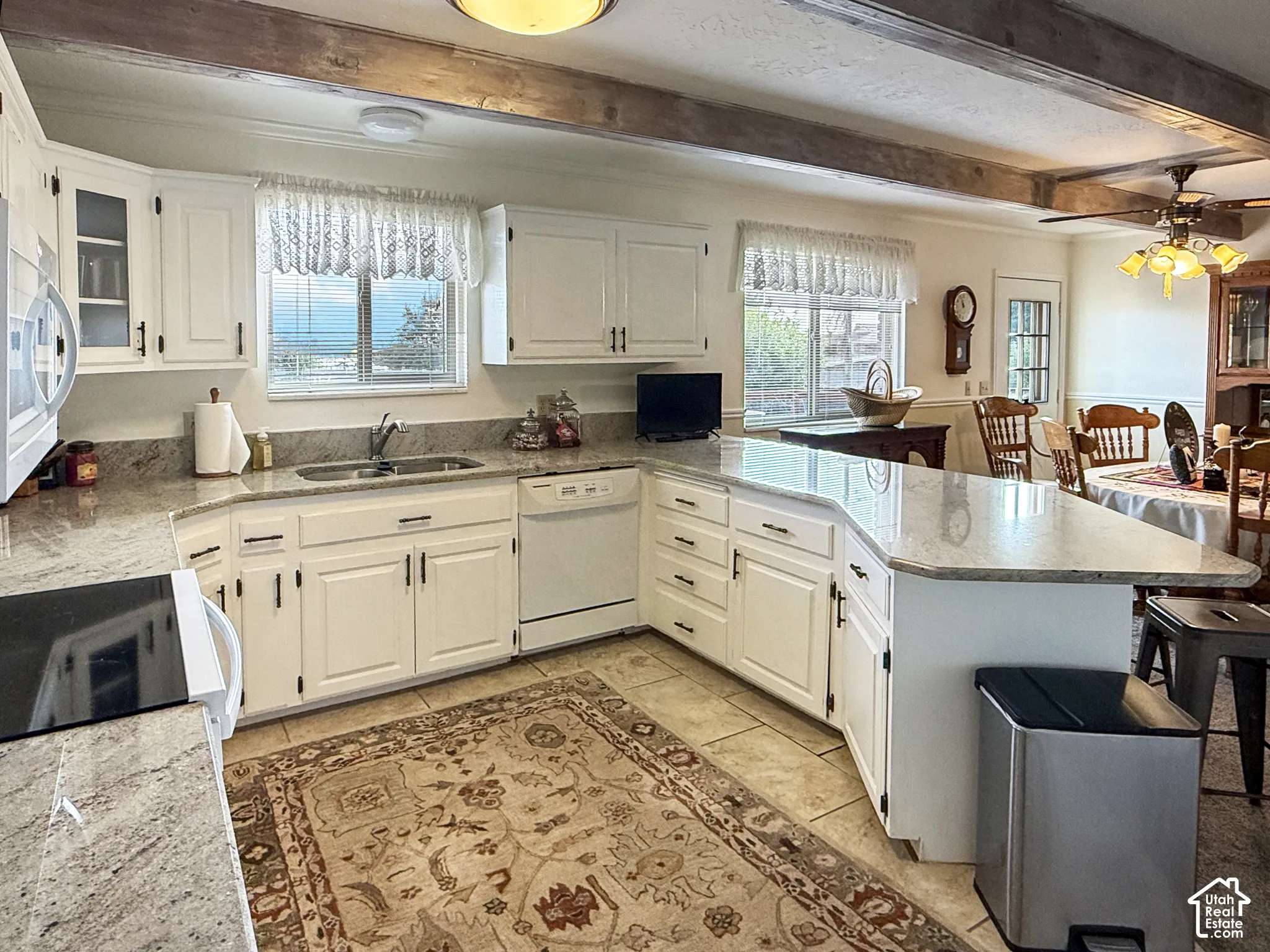 Kitchen featuring white cabinetry, stone countertops, a peninsula with extended counter space, tile flooring, and exposed wooden ceiling beams