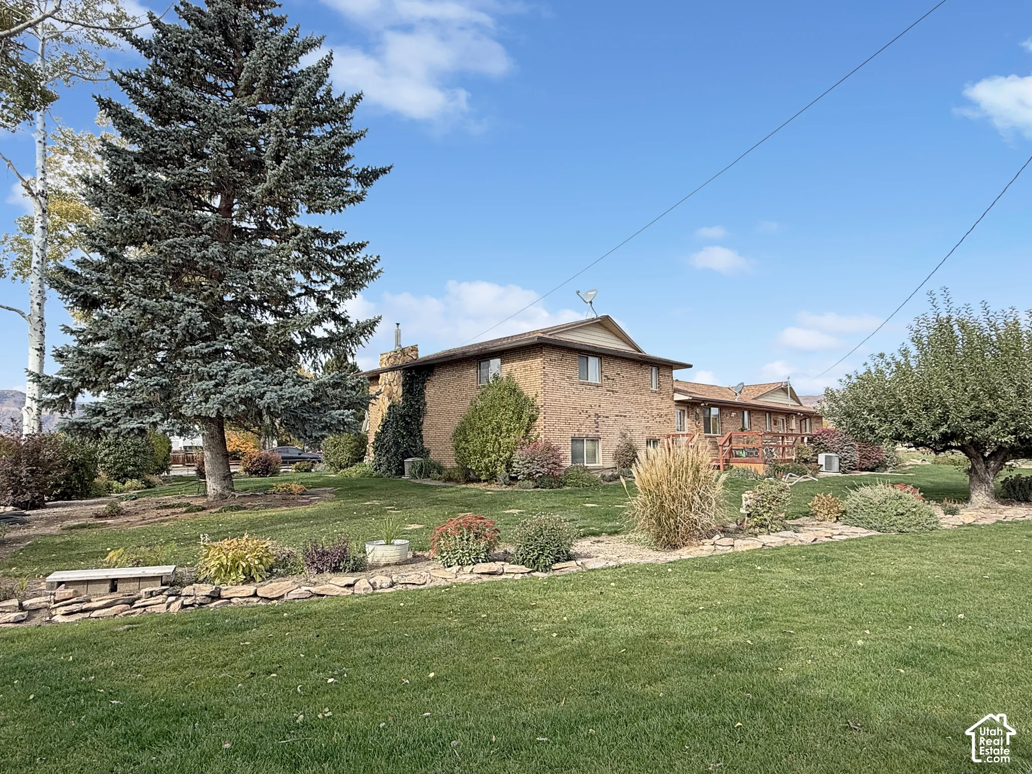 Brick exterior with stone accents, elevated wood deck, mature evergreen landscaping, and terraced stone retaining walls