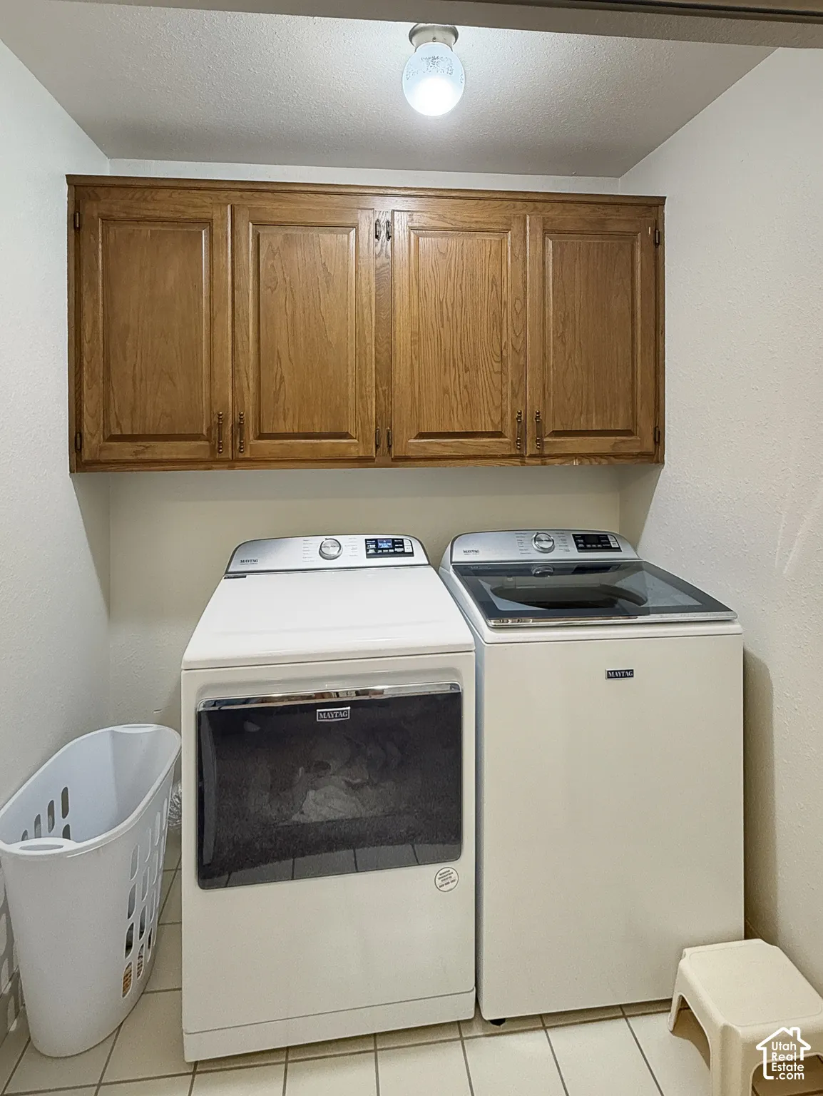 Laundry area featuring wood-finish cabinetry, tile flooring, and overhead lighting