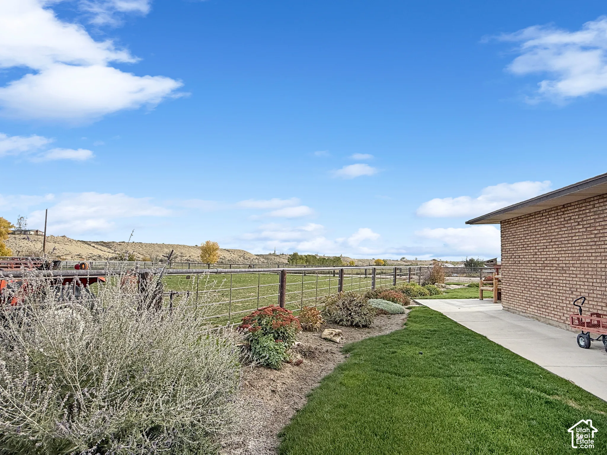 Expansive exterior grounds featuring a brick siding finish, a concrete patio, and wire-mesh fencing bordering an open field