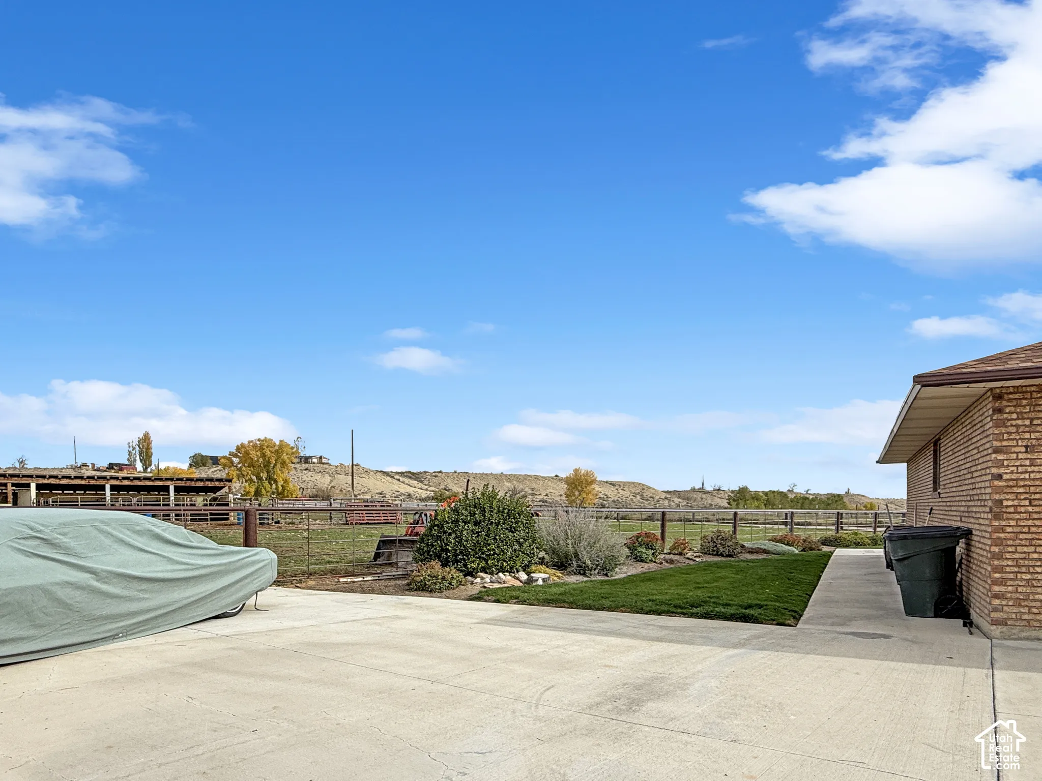 Expansive outdoor lot featuring brick siding, concrete parking area, manicured lawn, and perimeter wire fencing