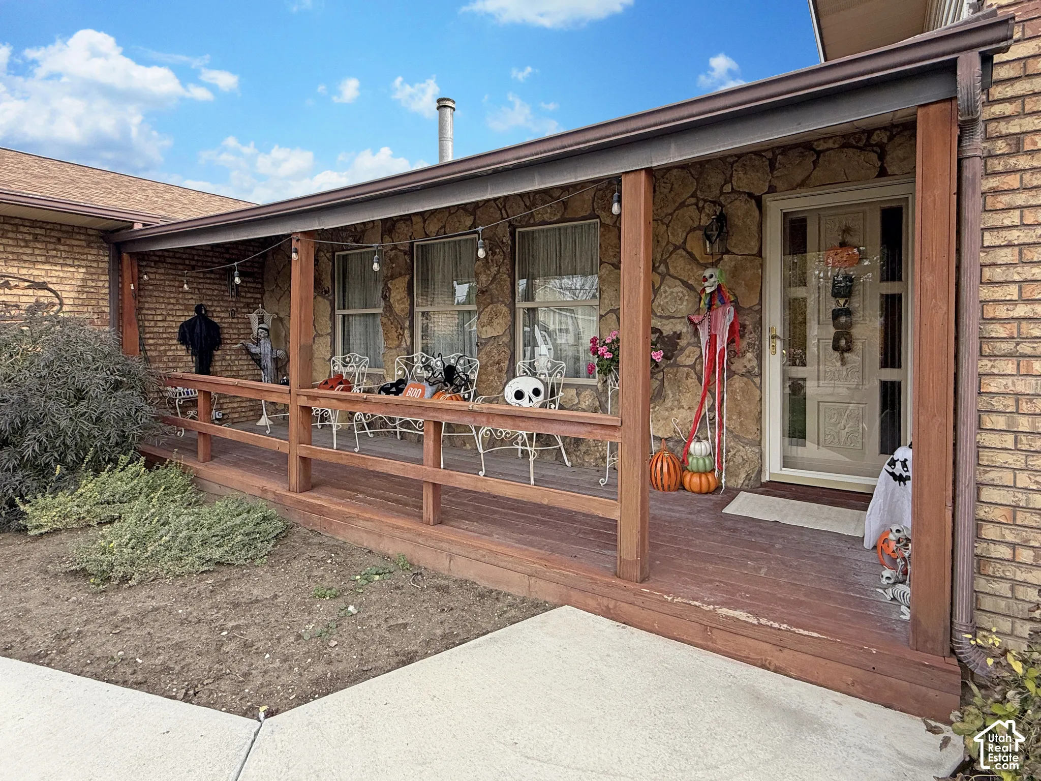 Covered wooden porch featuring natural stone facade accents and a light-toned door with glass paneling