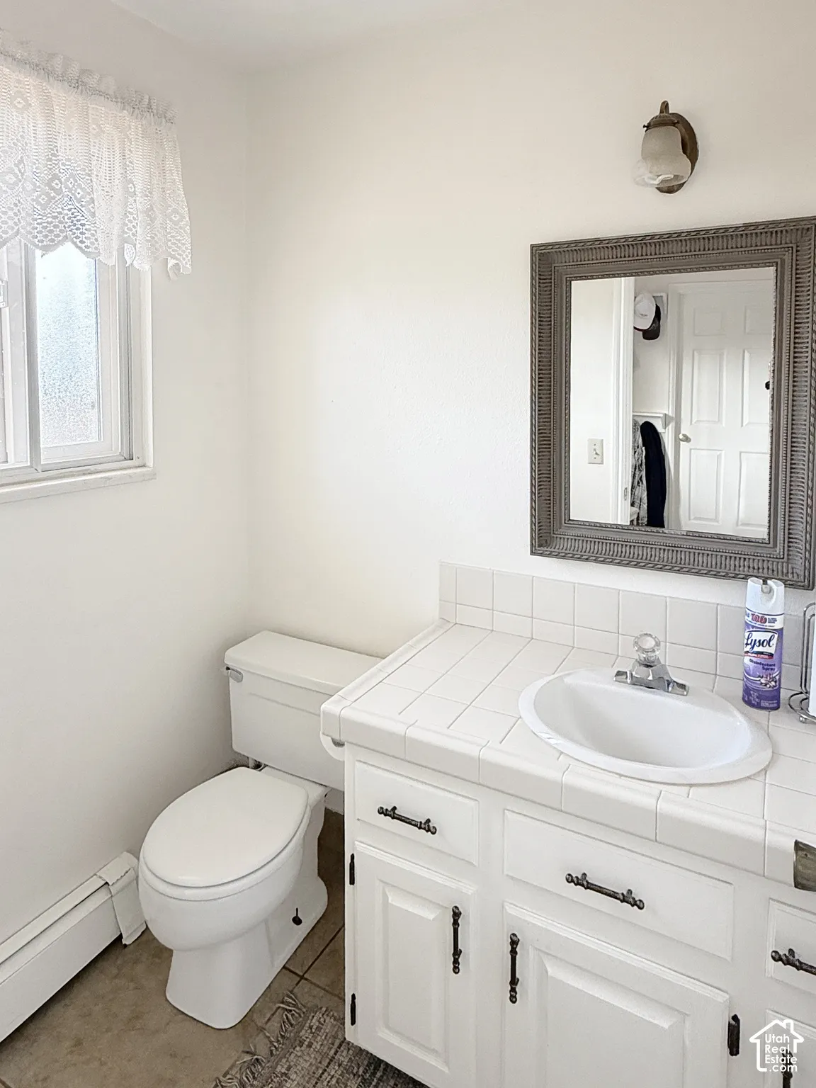 White tile countertop with an integrated oval sink, white cabinetry with dark metal hardware, and a single wall-mounted light fixture