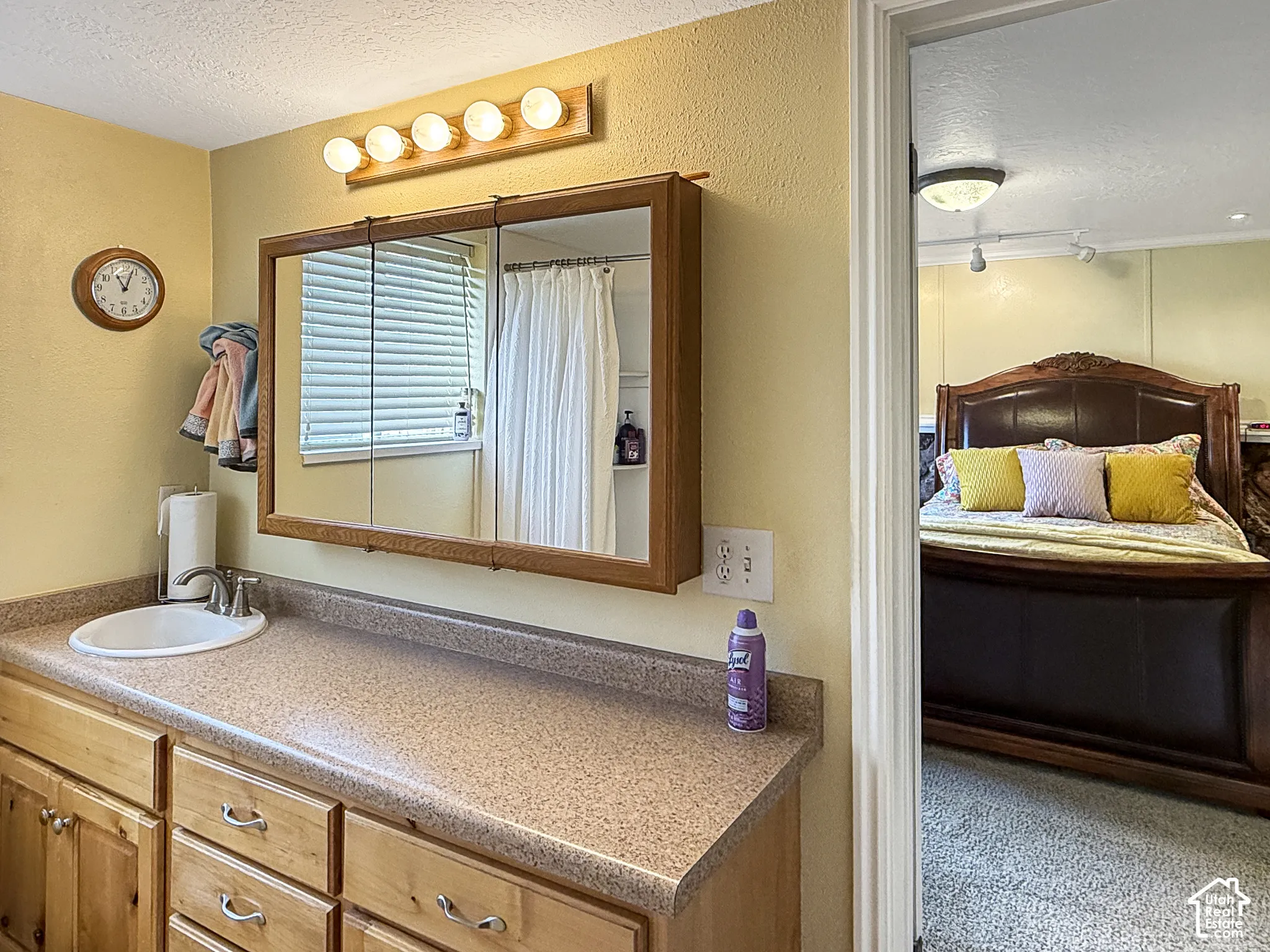 Bathroom featuring a wood-tone vanity, solid-surface countertop with an integrated basin, three-panel medicine cabinet, and a multi-bulb light fixture