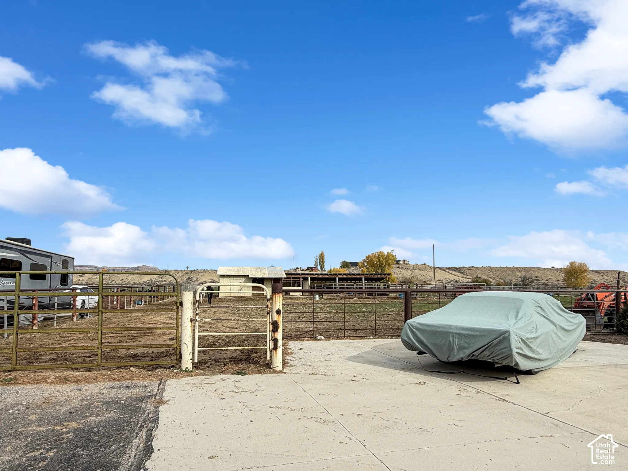 Expansive outdoor acreage featuring a concrete apron, metal tubular fencing, and a multi-stall covered structure