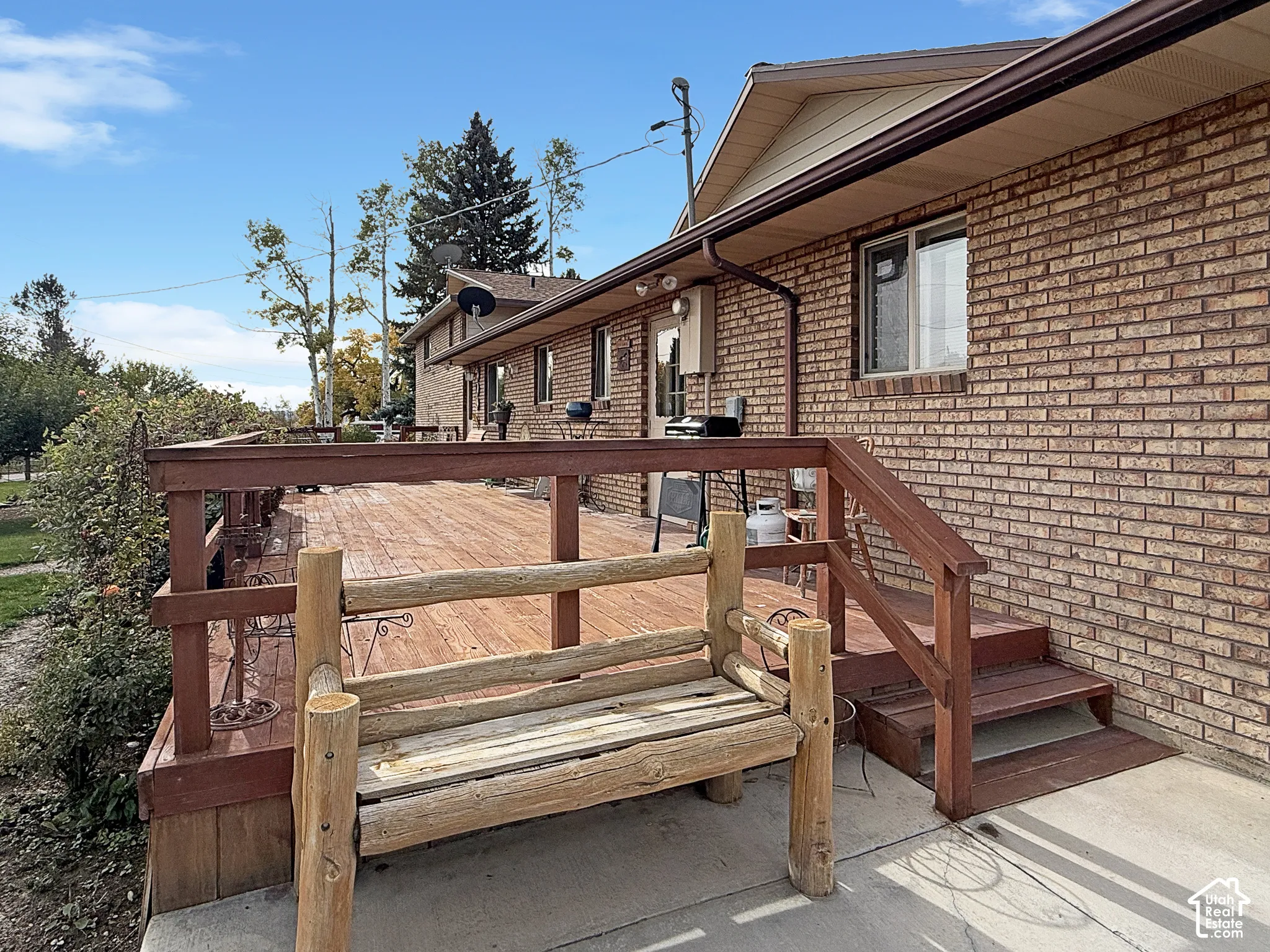 Expansive wood-decking with horizontal railings and integrated staircase, brick exterior, and concrete patio