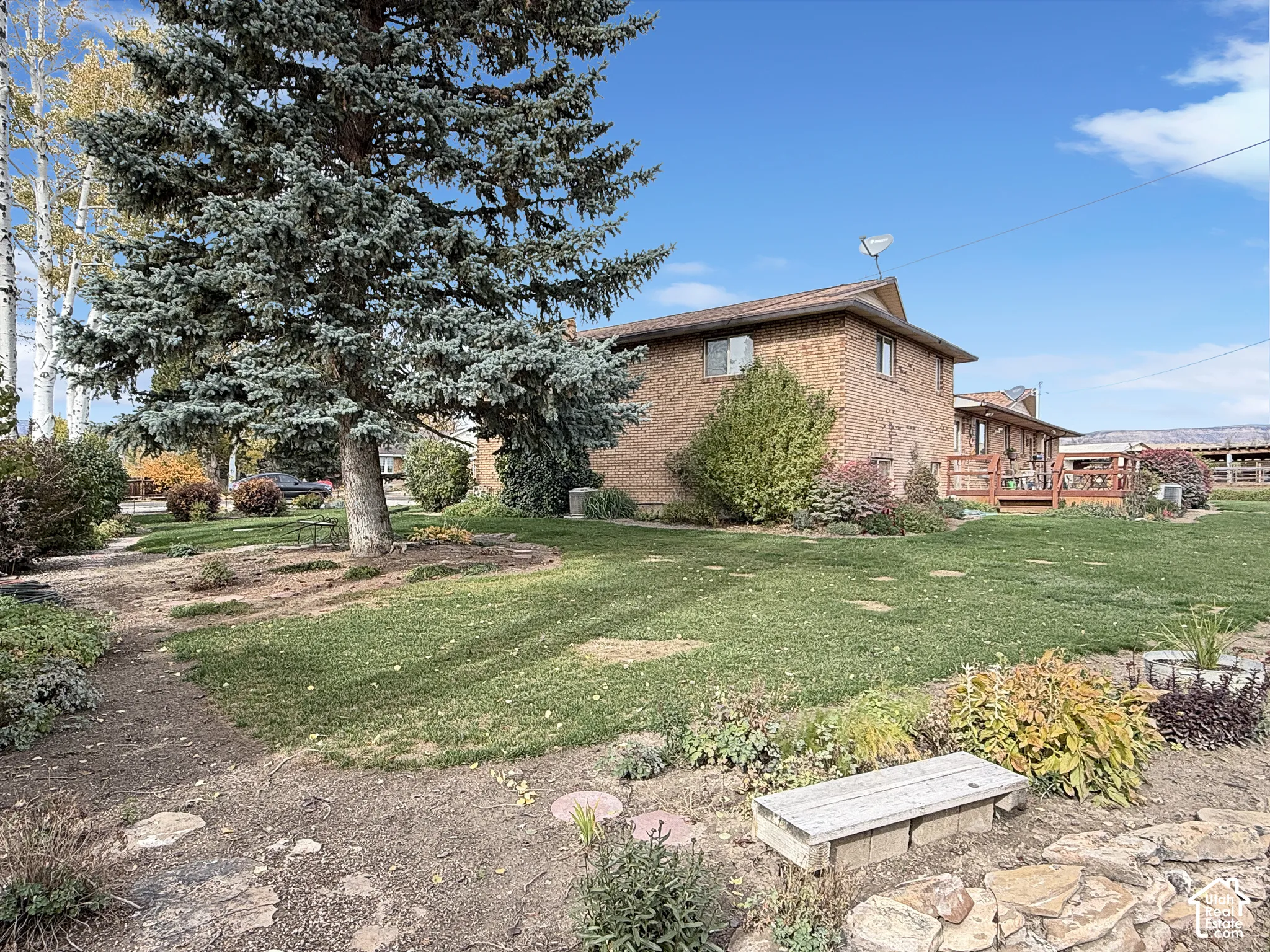 Brick exterior residence featuring mature pine trees, extensive landscaping, a stone retaining wall, and a raised wooden deck