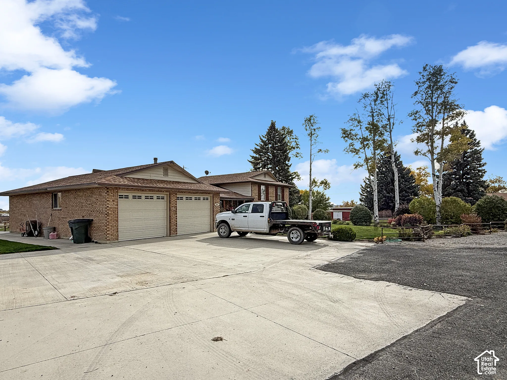 Brick exterior residence featuring an attached two-car garage, expansive concrete driveway, and mature landscaping