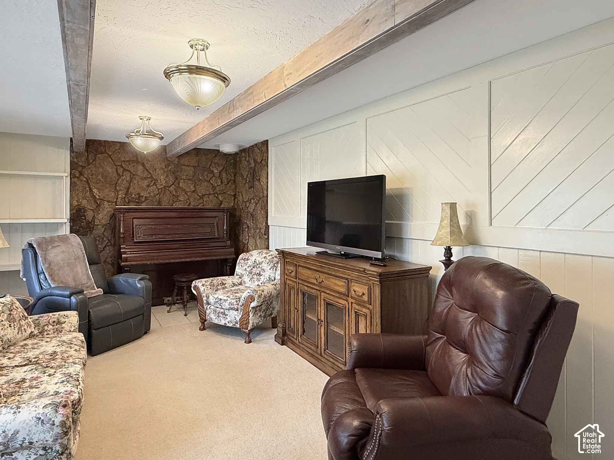 Interior room featuring textured stone accent wall, exposed wood ceiling beams, decorative wall paneling, and dual semi-flush mount lighting fixtures