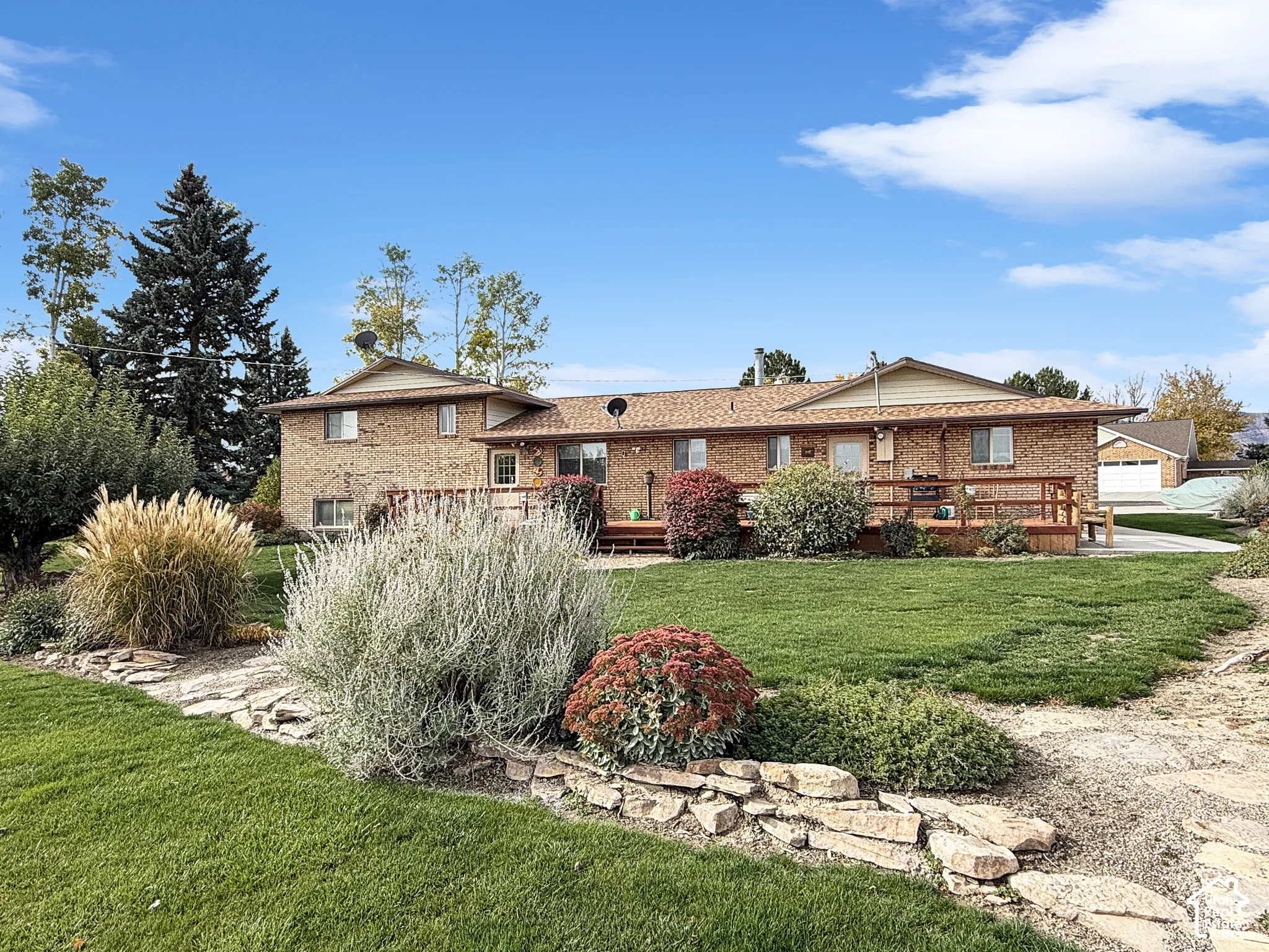 Brick exterior home featuring a raised wooden deck, stone-lined garden beds, and expansive lawn area