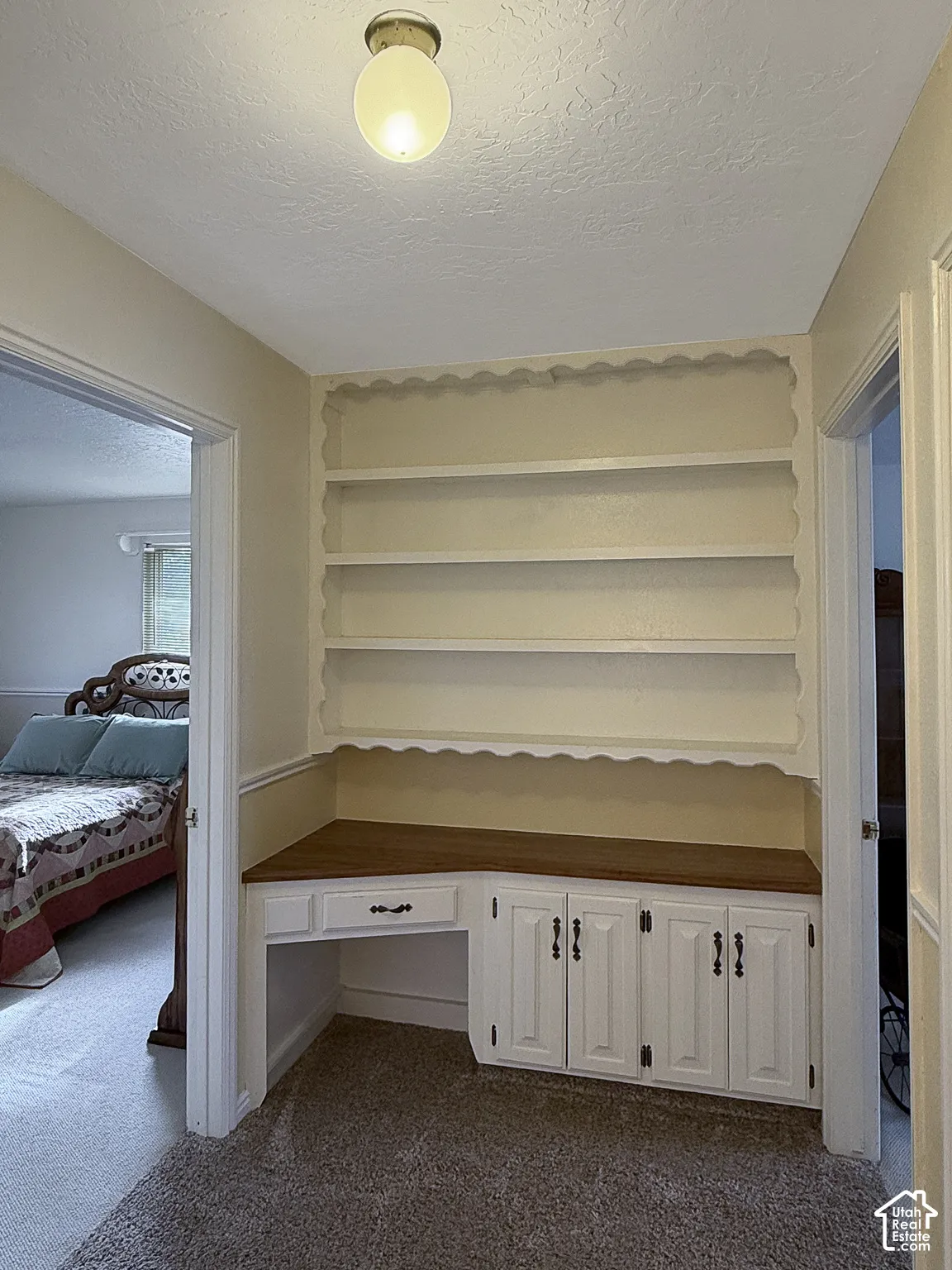 Built-in workstation featuring white cabinetry with dark hardware, wood-finish countertop, and scalloped-edge shelving