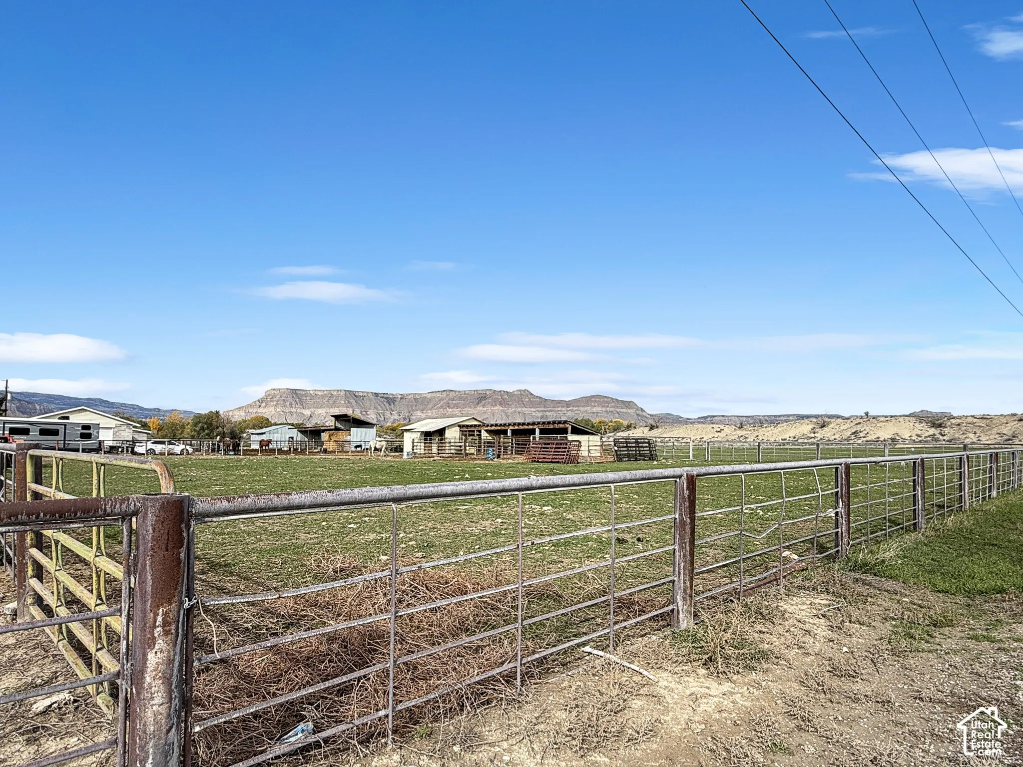 Expansive acreage featuring metal perimeter fencing, gated access, multiple outbuildings, and mountain terrain backdrop