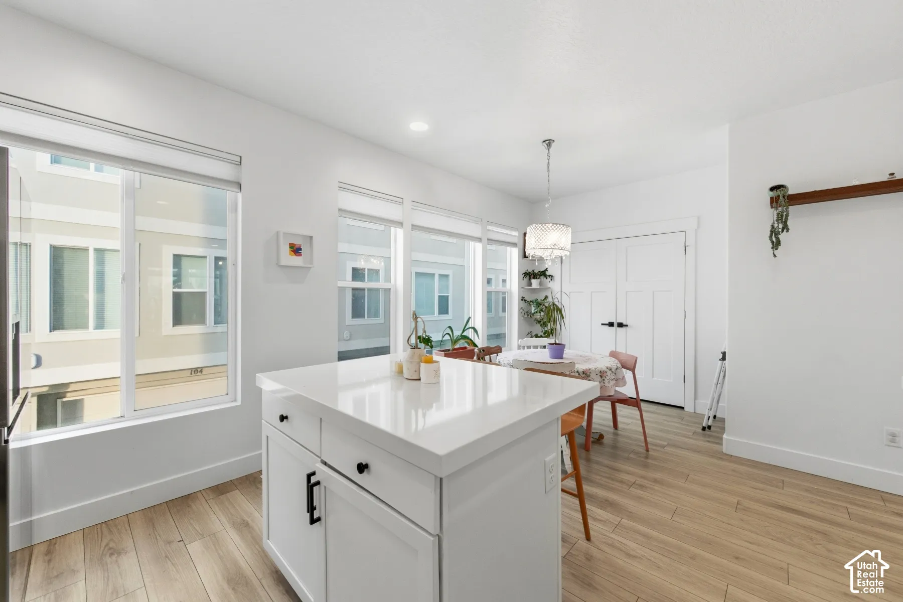 Kitchen featuring a central island with a solid surface countertop, white cabinetry with matte black hardware, wood-finish flooring, recessed lighting, and large windows with roller shades
