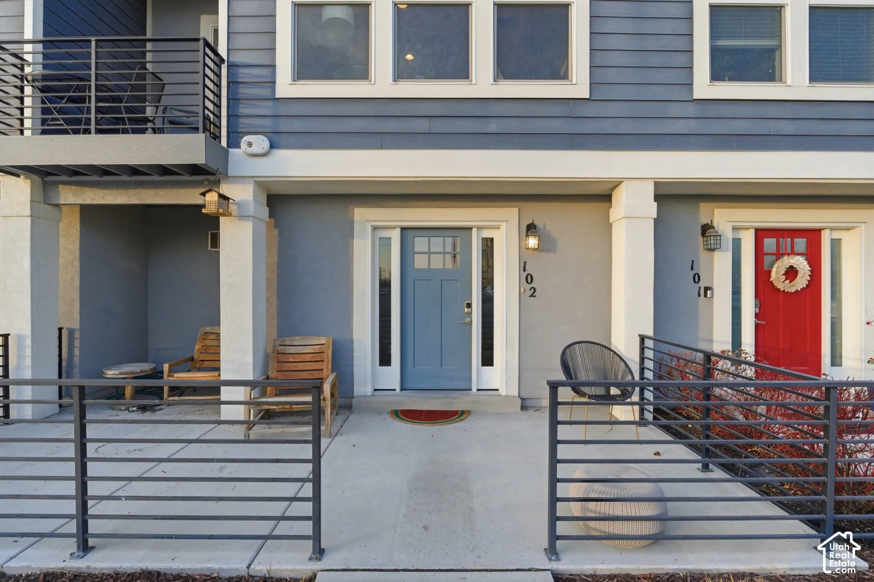 Exterior facade featuring multi-tone horizontal siding, concrete front patio, metal horizontal rail fencing, and exterior wall-mounted light fixtures