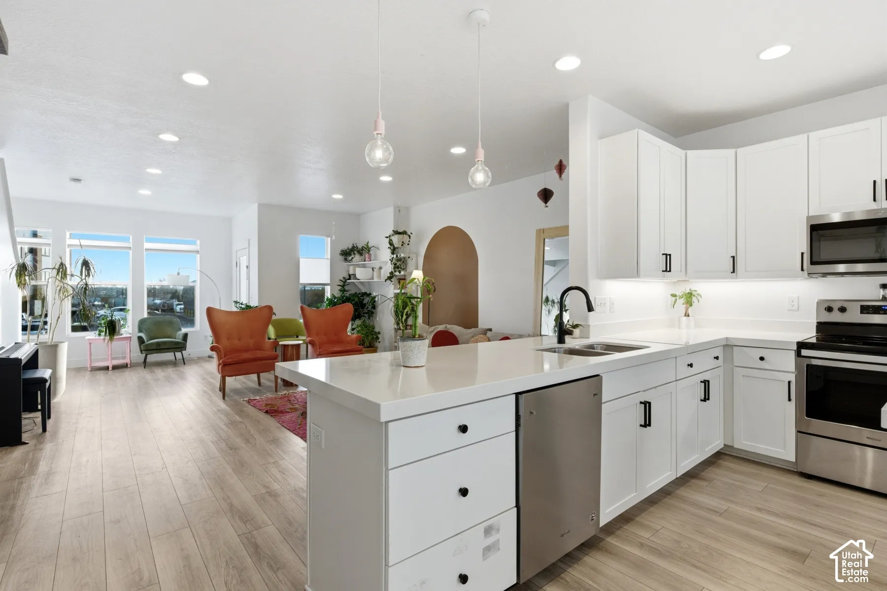 Kitchen featuring white shaker-style cabinetry, quartz countertops, stainless steel appliances, dual pendant lighting, and wood-finish flooring