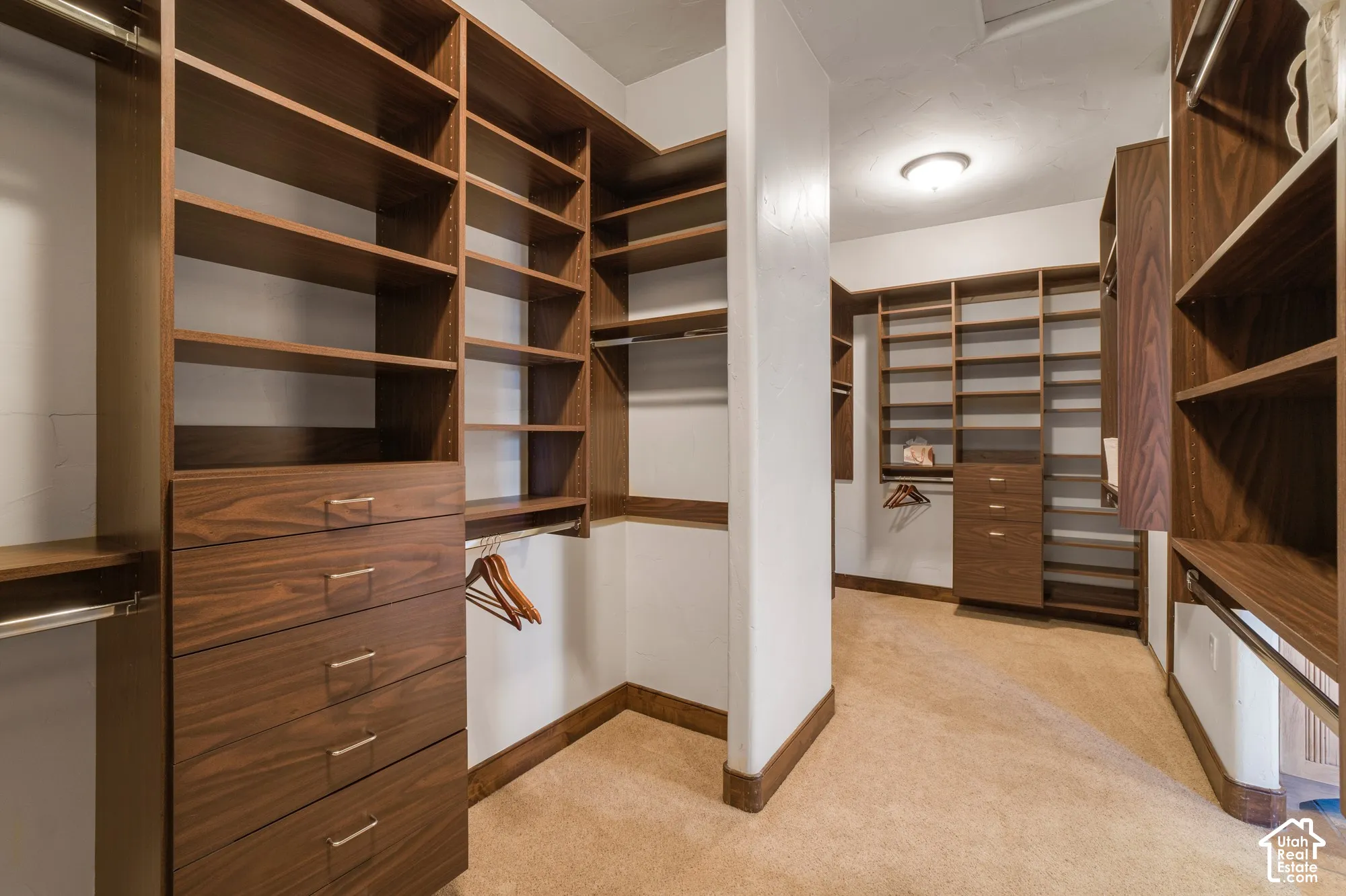 Walk-in closet featuring extensive built-in wood-finish shelving, integrated storage drawers with metal hardware, and multiple hanging rods