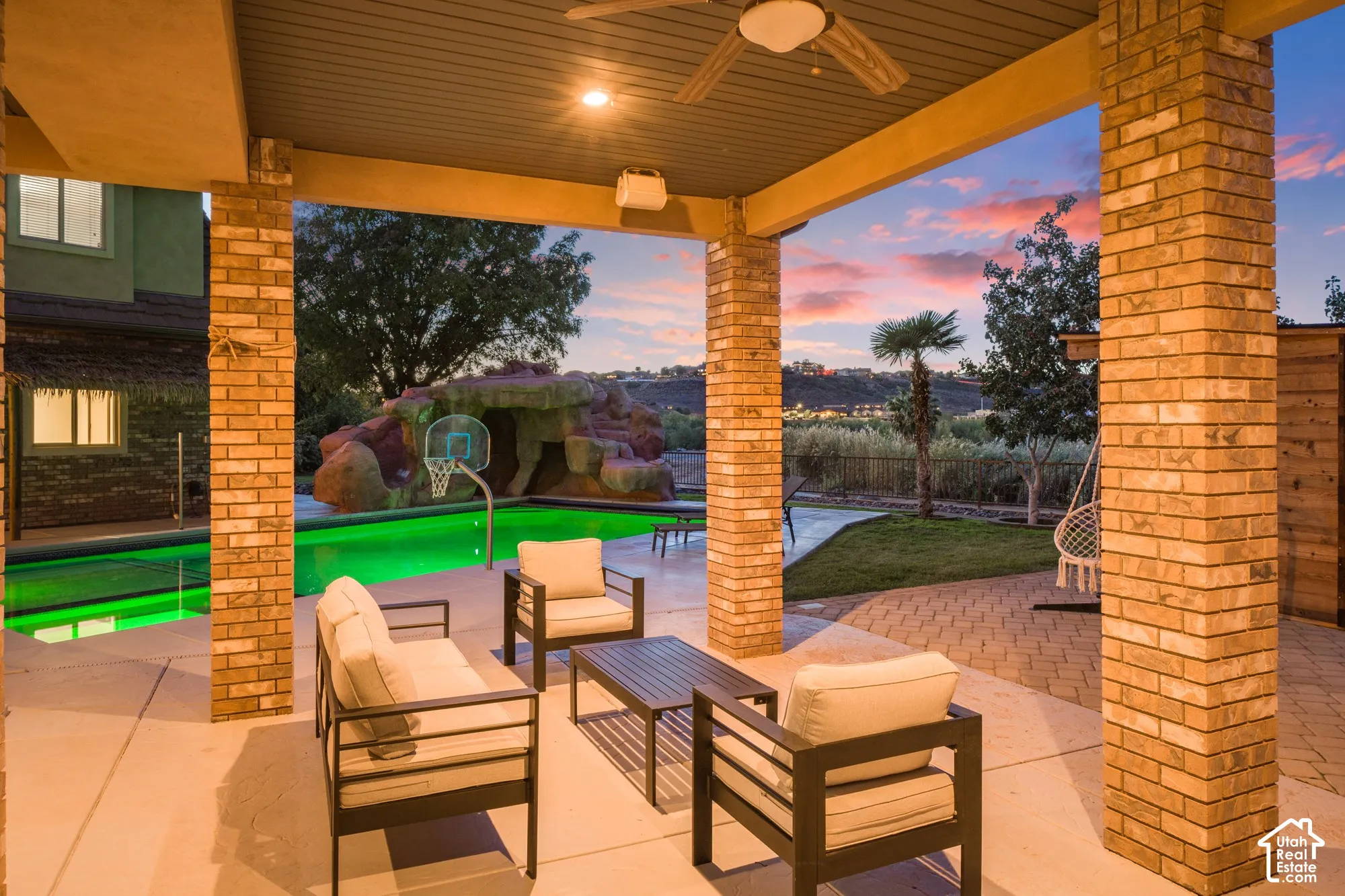 Covered patio featuring brick support columns, recessed ceiling lighting, a ceiling fan, and a concrete floor, overlooking a swimming pool with a rock-feature slide and stone-paver decking