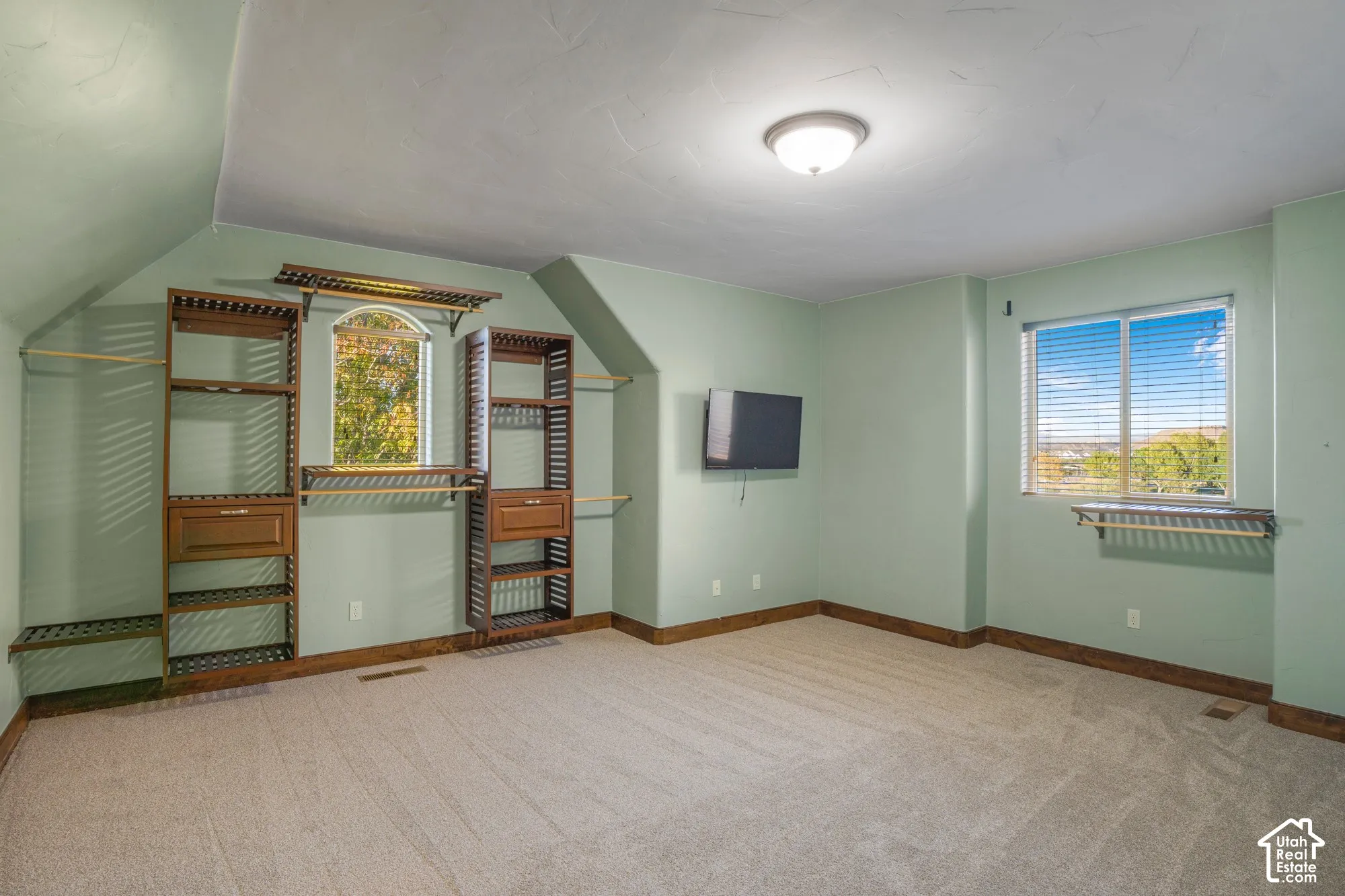 Room featuring vaulted ceilings, installed wall shelving with integrated drawers, carpeted flooring, and a window with exterior scenery