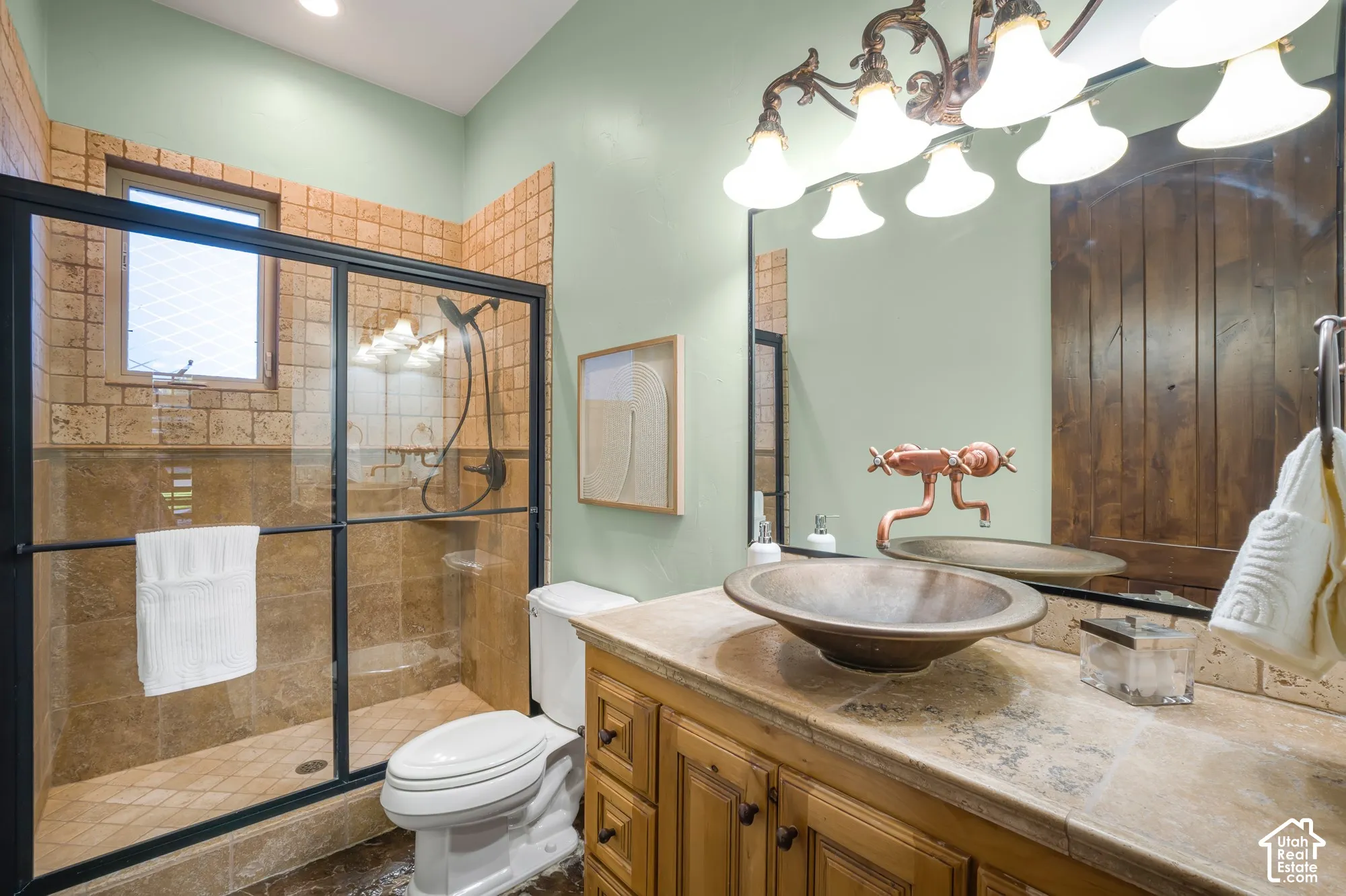 Bathroom featuring a vessel sink with wall-mounted plumbing fixtures, stone countertop, custom cabinetry, walk-in shower with stone tile surround, and an integrated lighting fixture