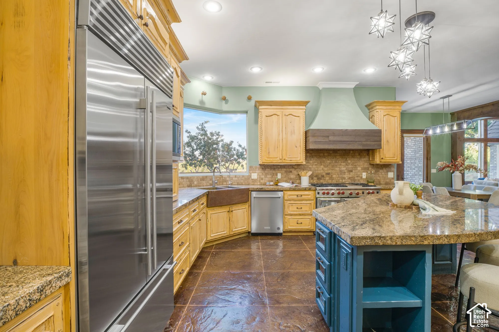 Kitchen featuring a stainless steel built-in refrigerator, stone-topped central island with built-in cabinetry, custom wood range hood, copper-finish apron-front sink, and tile flooring