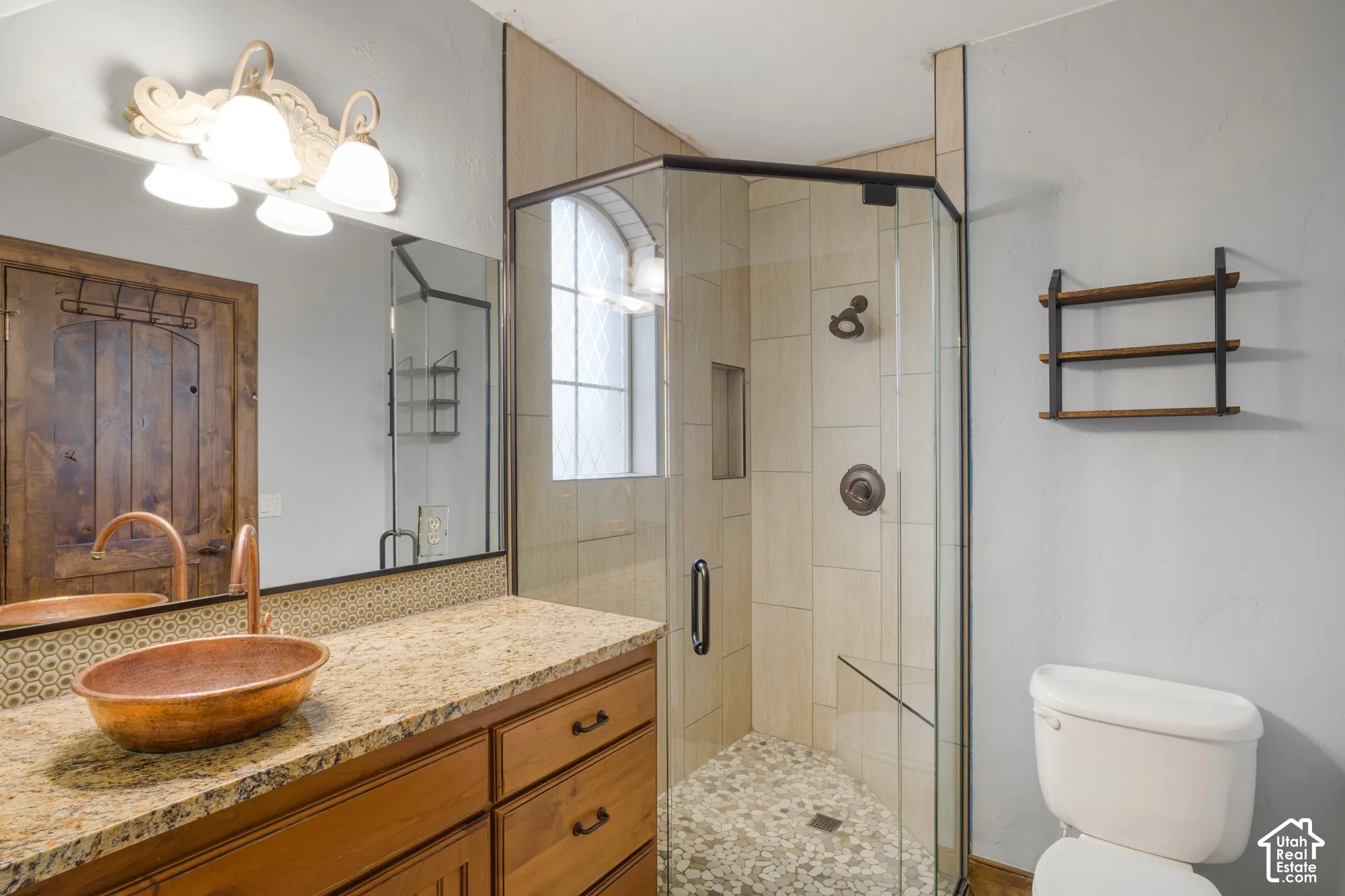 Vanity featuring a stone-look countertop, a hammered copper vessel sink, and an arched-pane window within a glass-enclosed shower with a built-in bench