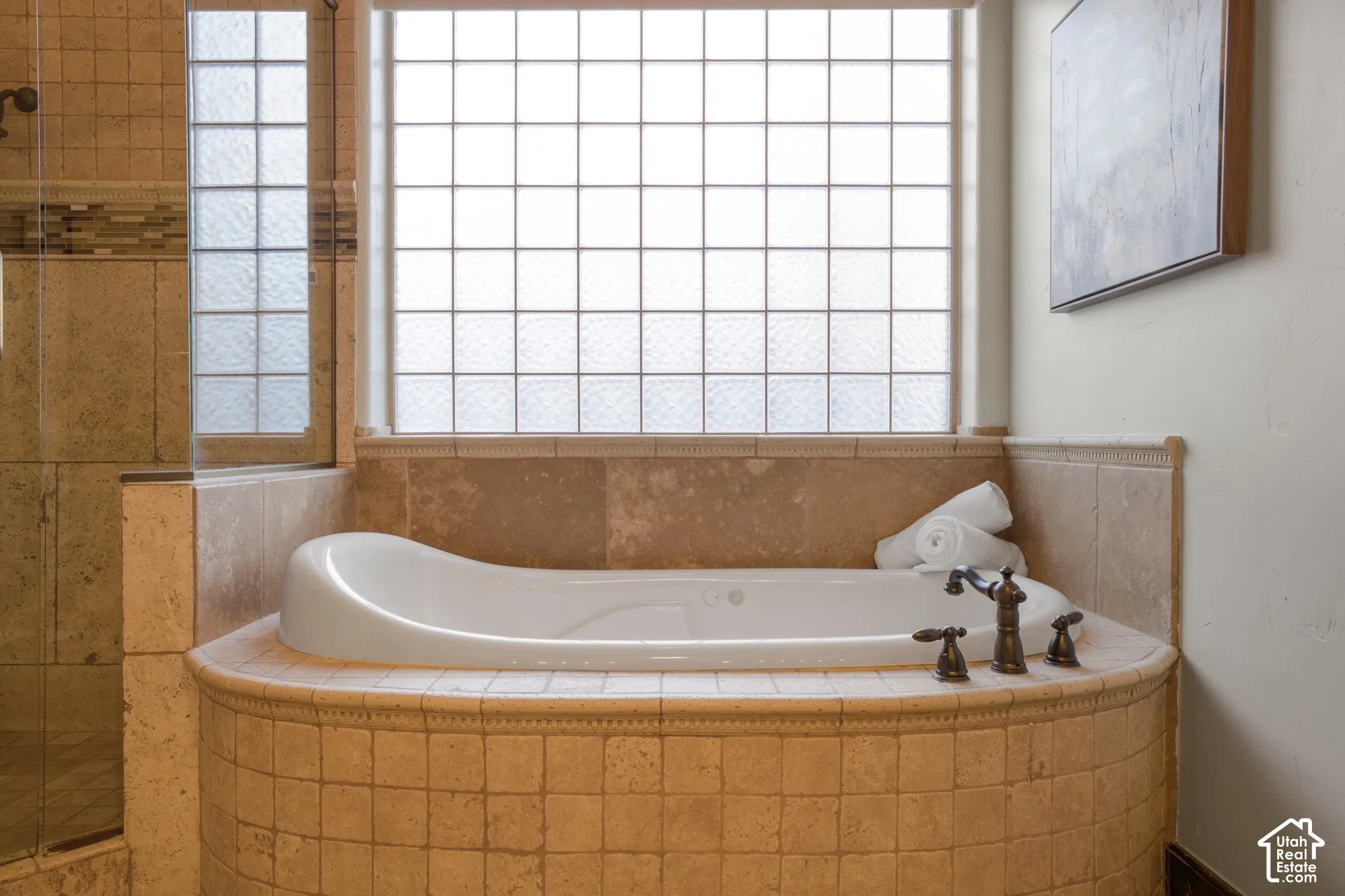Jetted soaking tub featuring a tile surround, decorative molding, glass block window, and oil-rubbed bronze fixtures