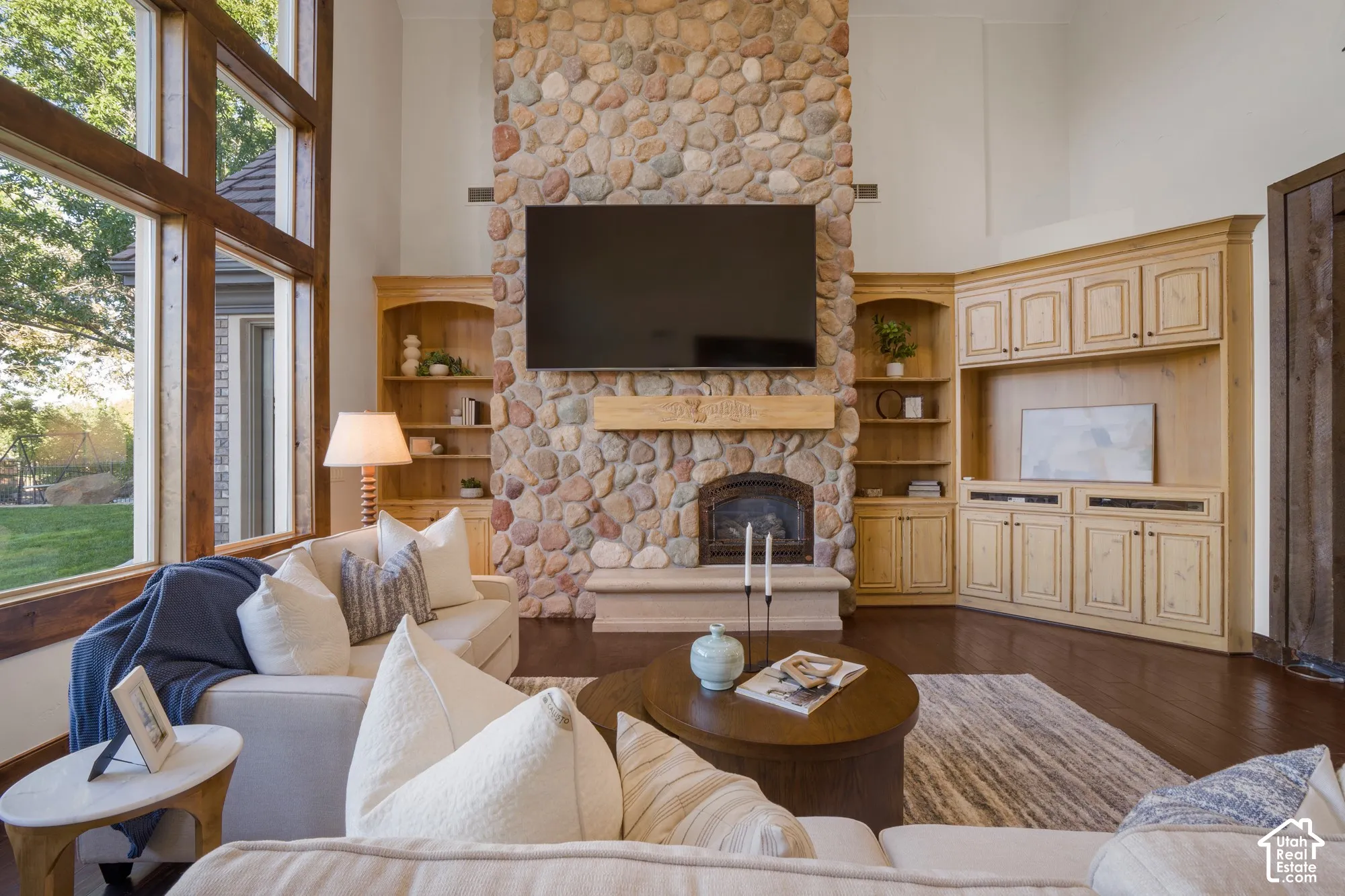 Floor-to-ceiling stone fireplace with a limestone hearth and wood mantel, expansive windows, and custom built-in cabinetry featuring wood-finish flooring