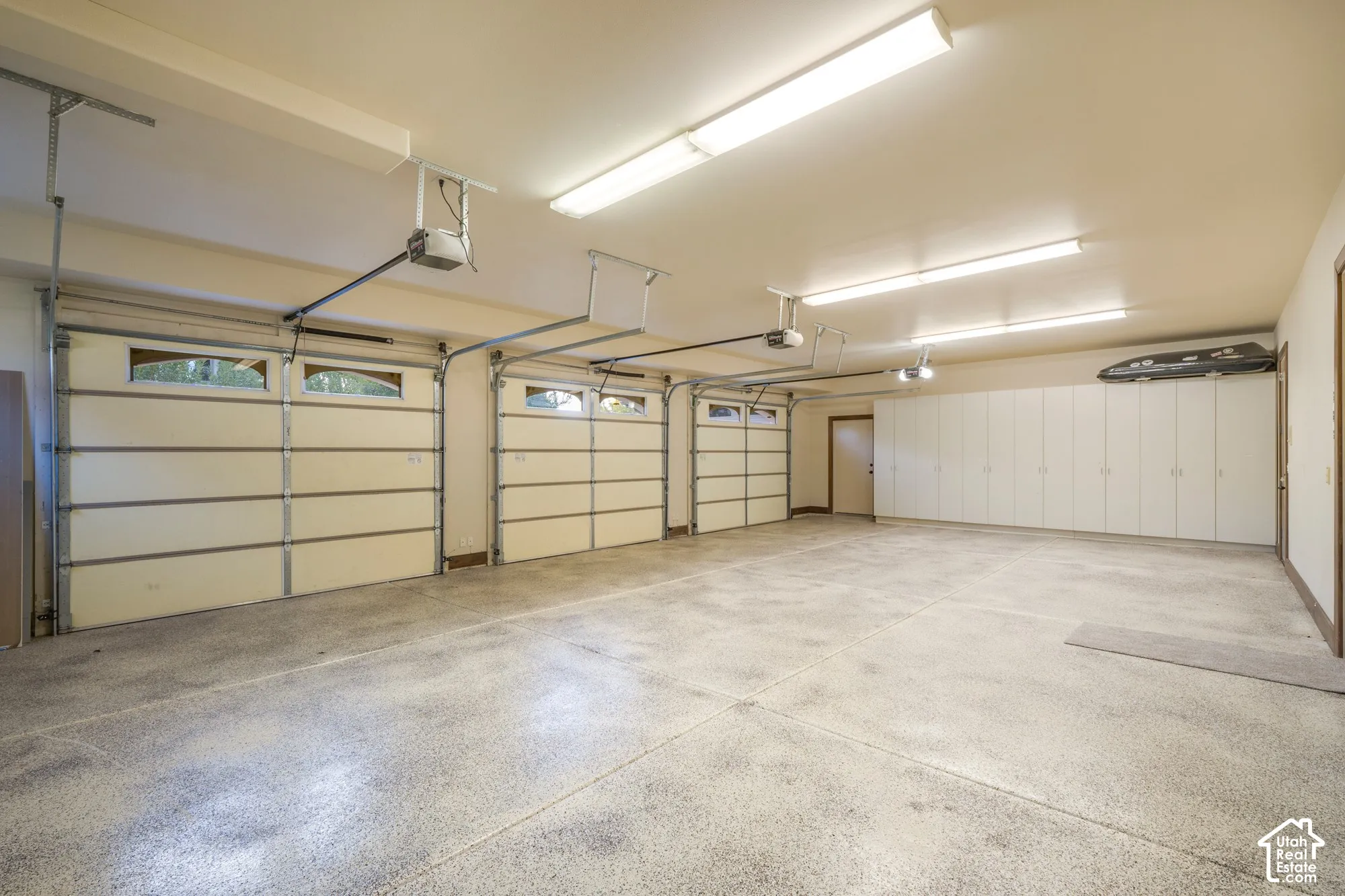 Three-car garage featuring segmented roll-up doors with glass inserts, epoxy-coated flooring, and floor-to-ceiling built-in storage cabinetry
