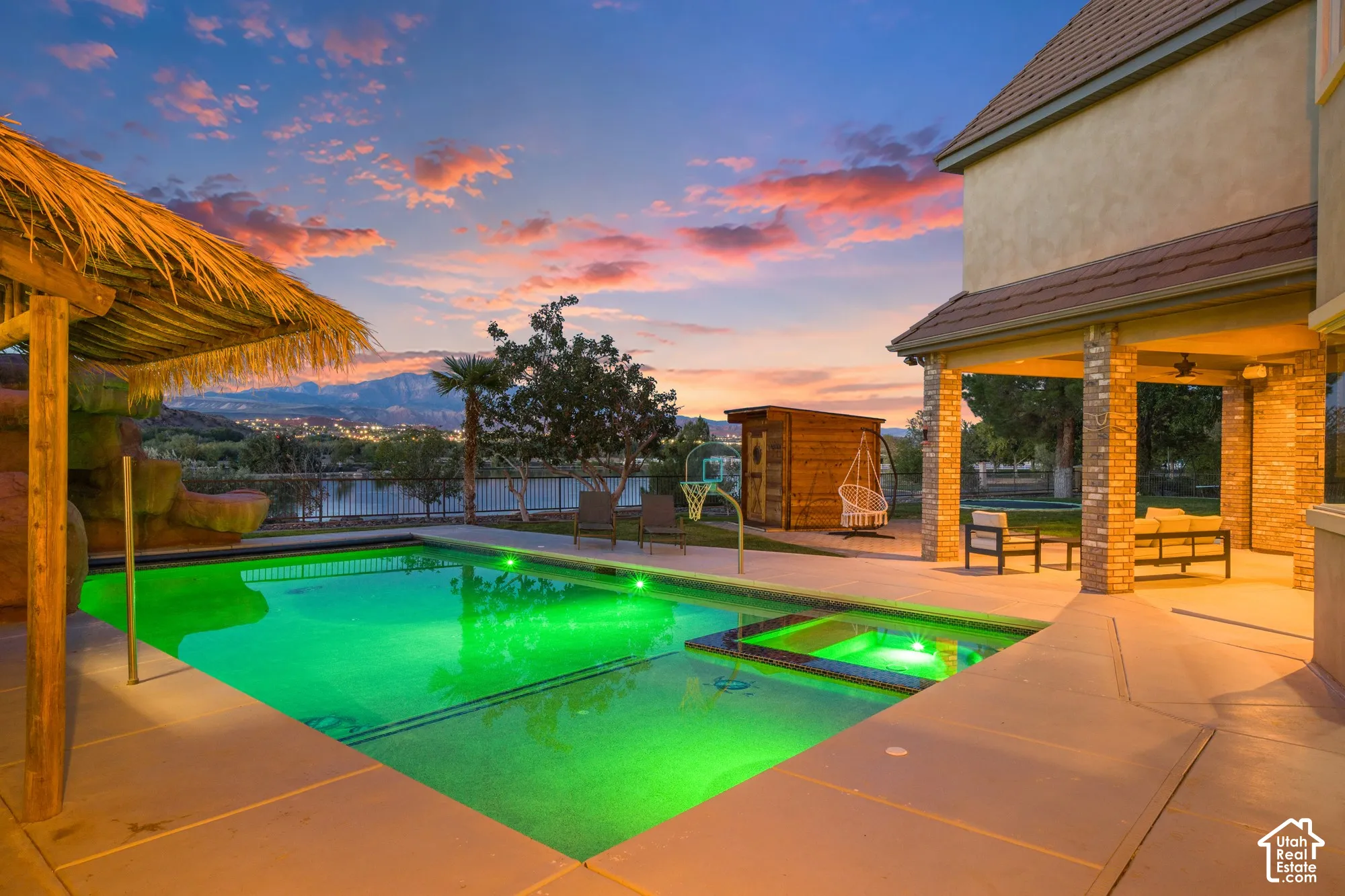 In-ground swimming pool with an integrated spa, covered brick patio, and thatched-roof poolside cabana
