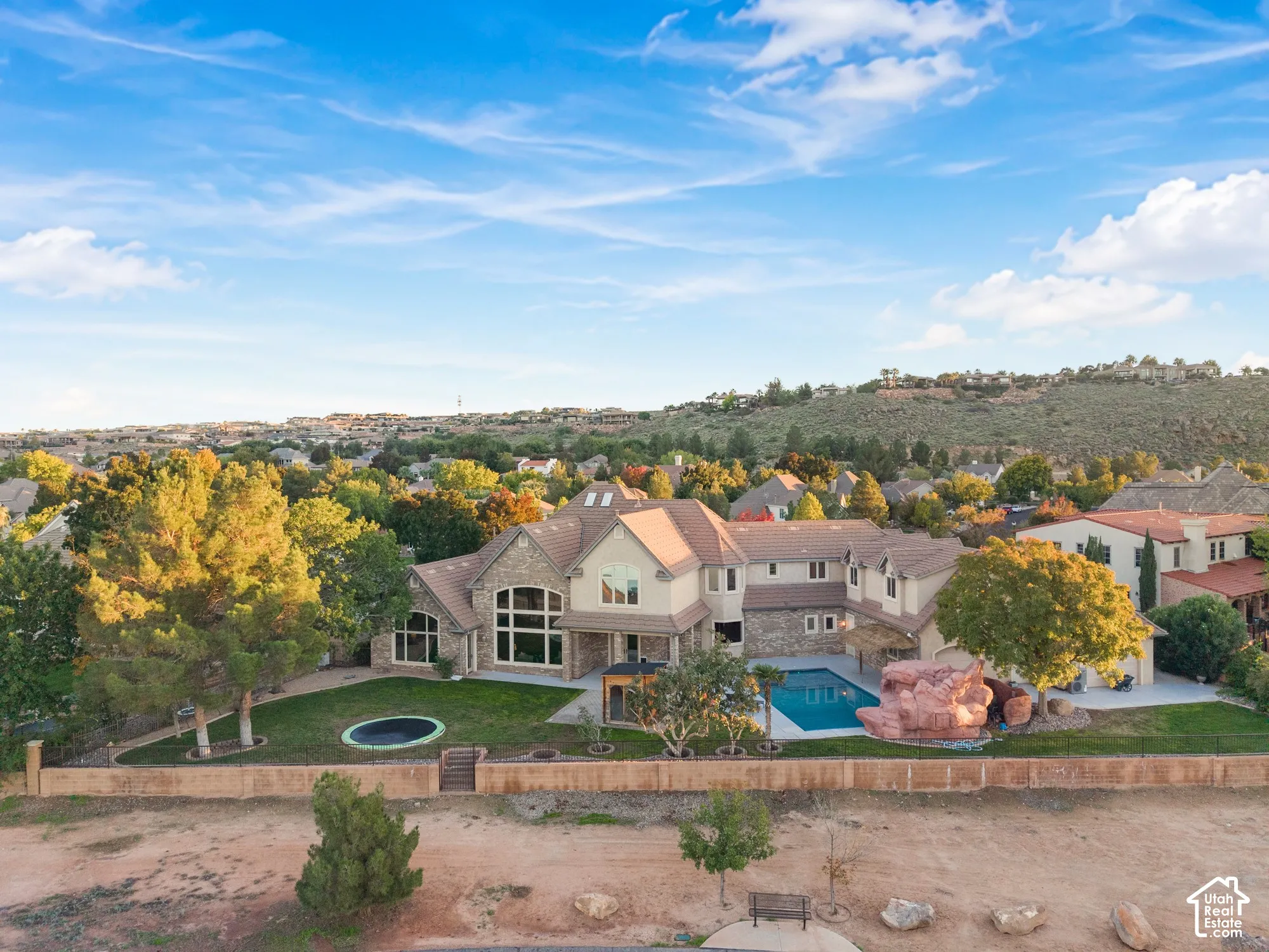 Multi-level residence featuring stone and stucco exterior, custom swimming pool, decorative rock formation, expansive lawn, and fenced perimeter