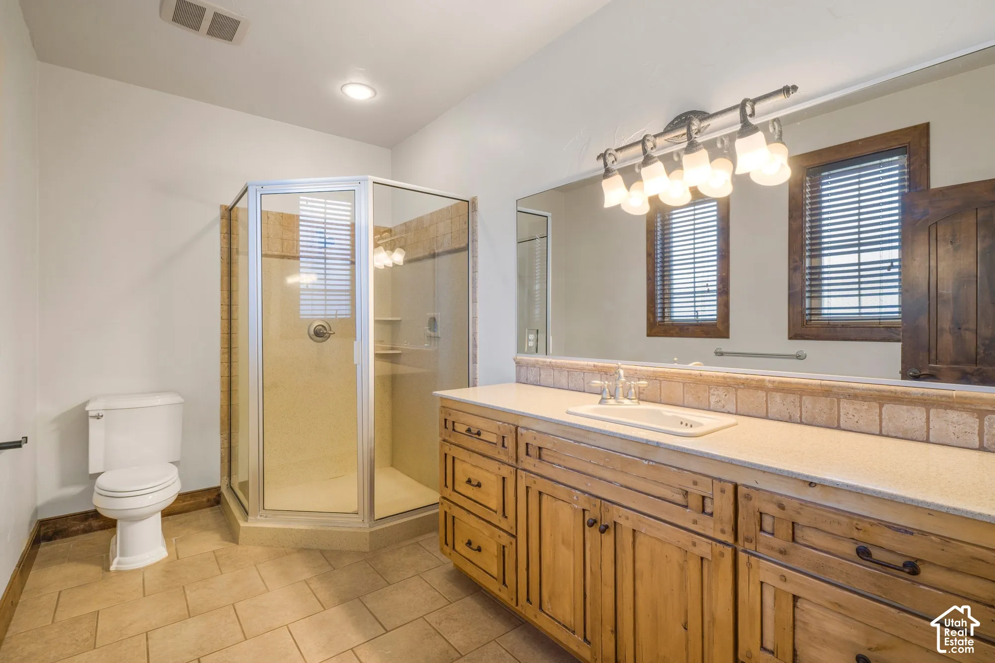 Bathroom featuring a stone-topped vanity with natural wood-finish cabinetry, a corner glass-enclosed shower with tiled surround, tile flooring, and a large wall-mounted mirror