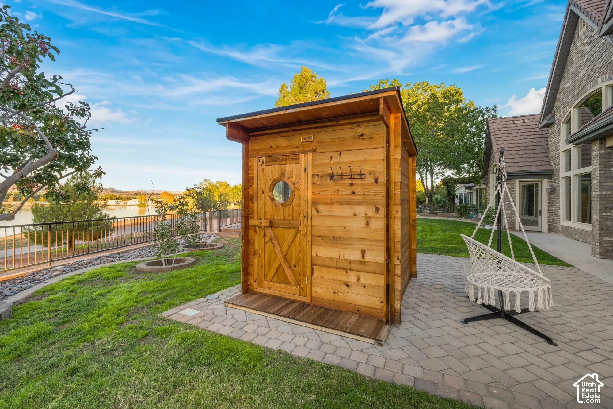 Detached cedar sauna featuring a porthole window, single-pitch roof, and integrated exterior hook rack, situated on a paved stone patio