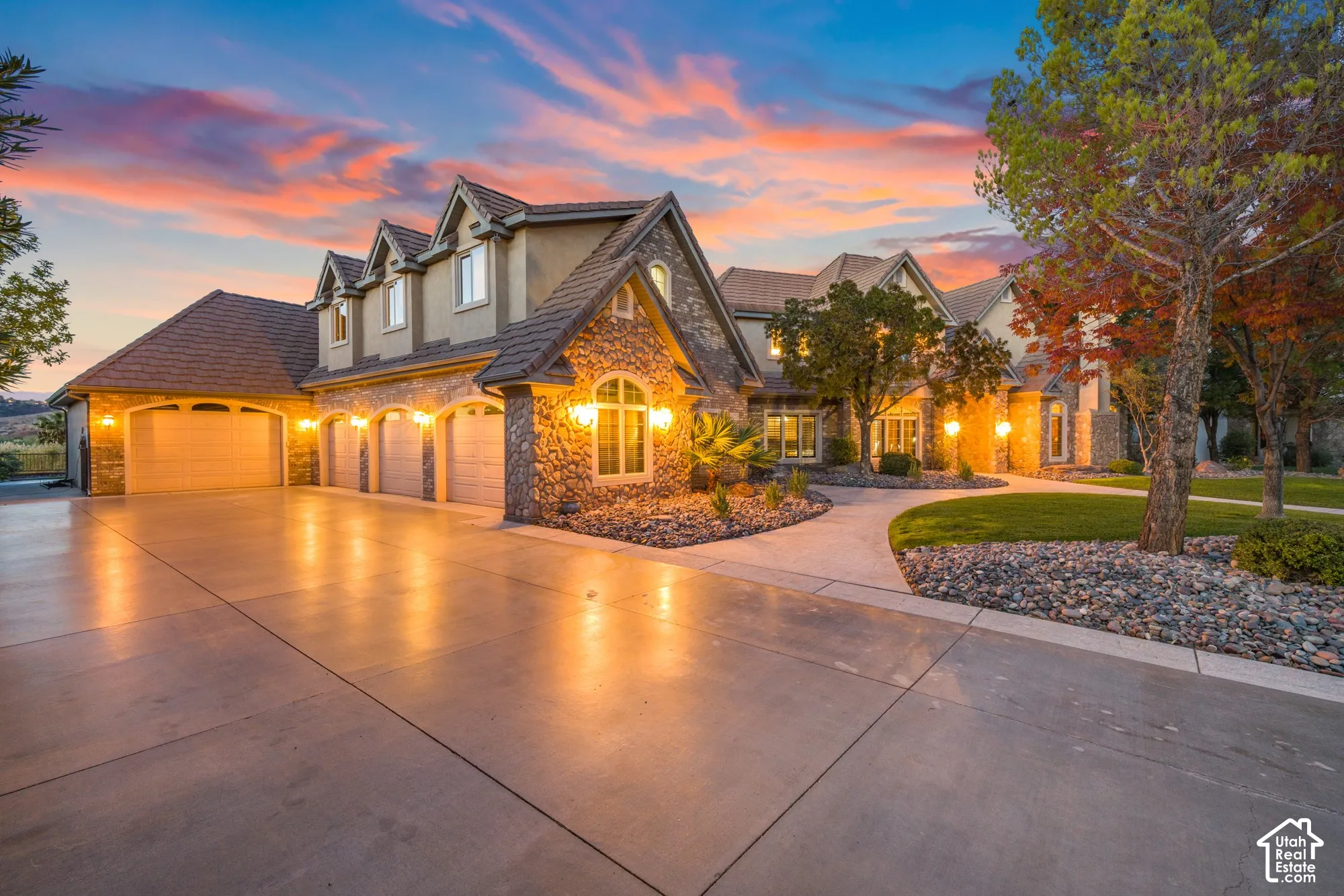 Multi-gabled exterior featuring stone masonry cladding, a four-car garage, concrete driveway, and professional xeriscaping