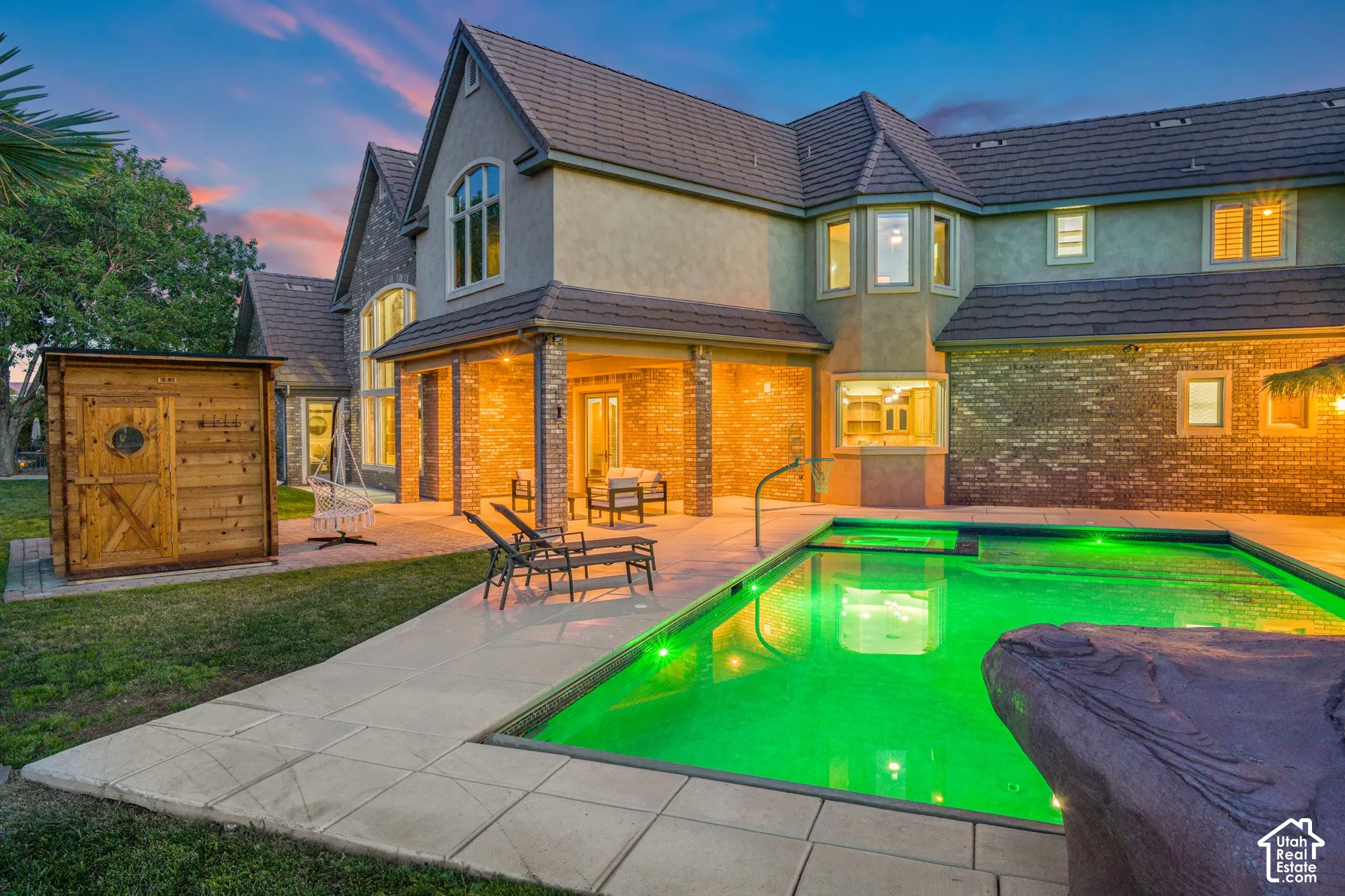 Multi-story residence featuring brick and stucco exterior, covered patio, in-ground pool with stone accent feature, and detached wood-construction structure