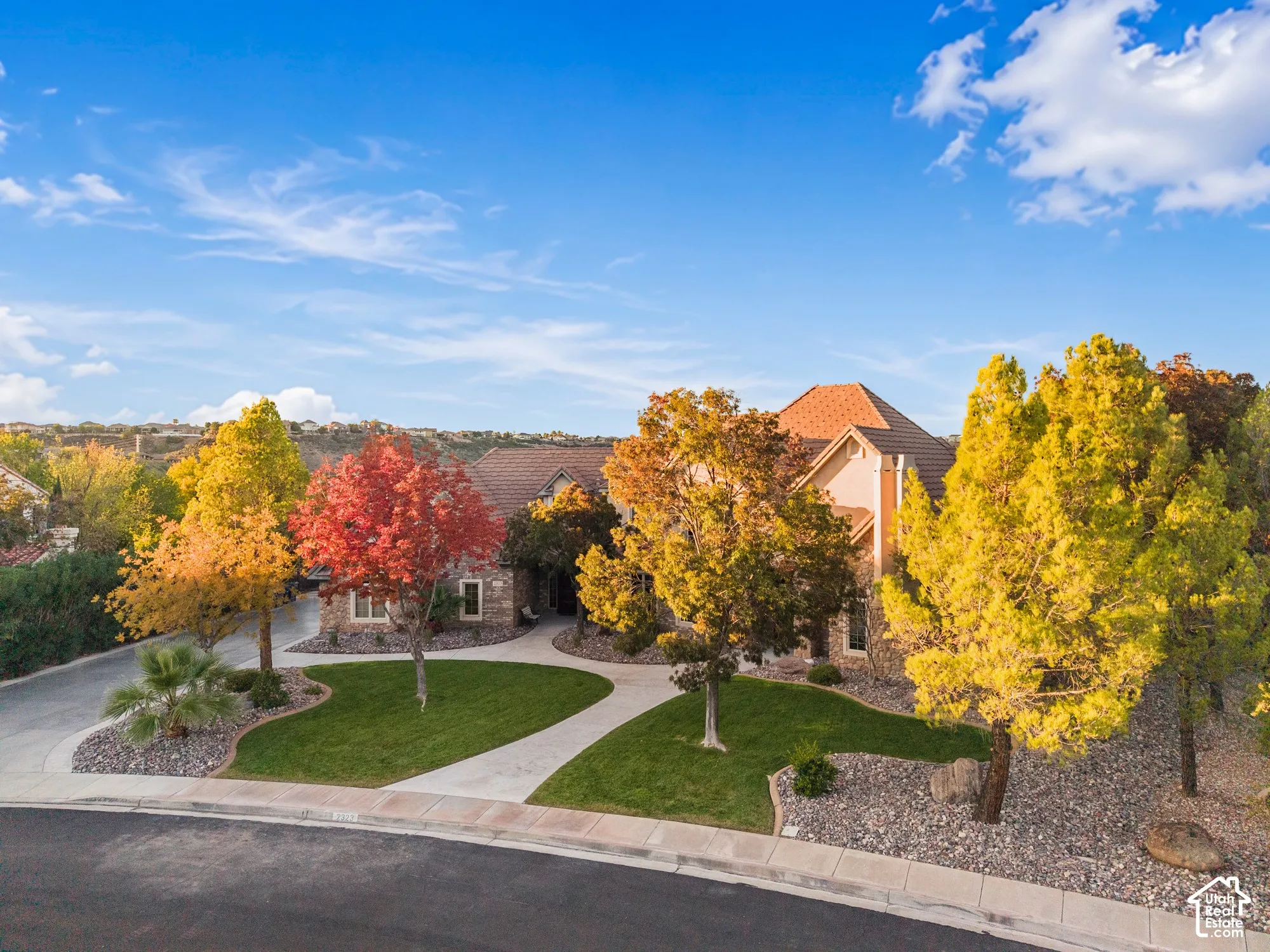 Multi-gabled residence with stone masonry facade, concrete tile roofing, manicured lawn, and curved concrete entryway