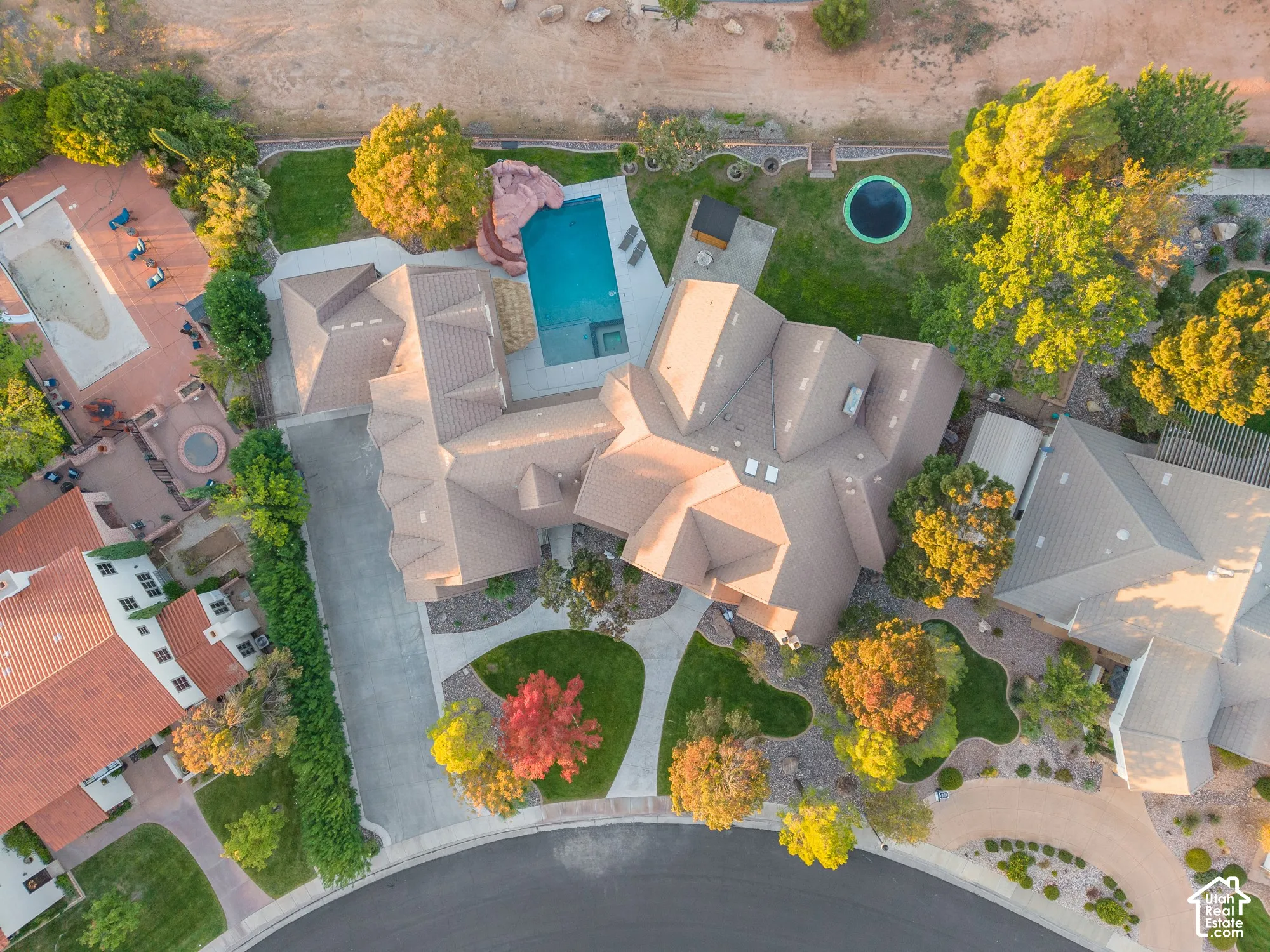 Aerial perspective featuring a multi-gabled roofline, concrete driveway, swimming pool with rock accent, and landscaped grounds with mature trees