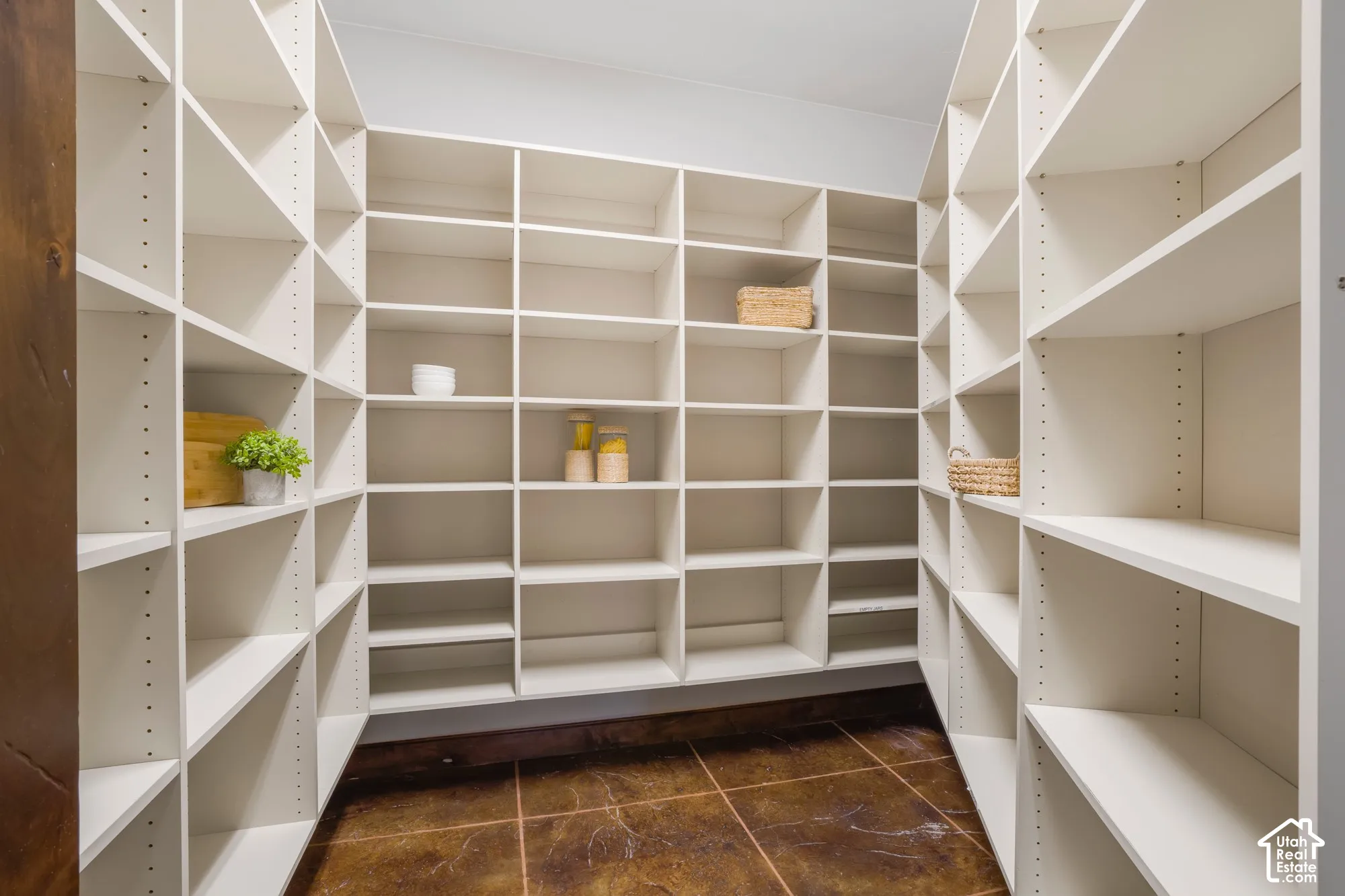 Walk-in storage space featuring extensive white floor-to-ceiling built-in shelving with adjustable hardware and dark stone-finish flooring