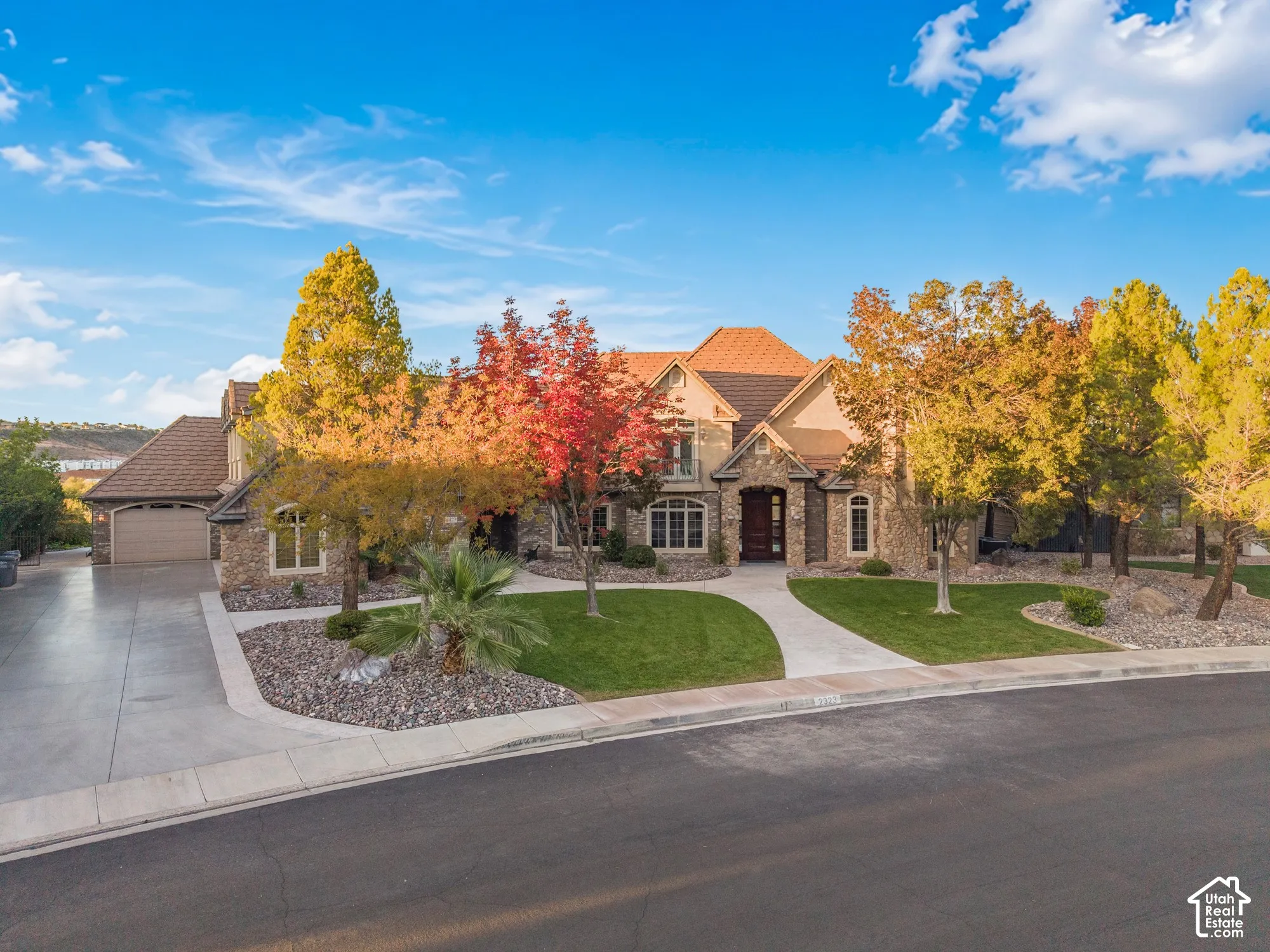 Multi-gabled exterior featuring stone masonry cladding, arched window detailing, multi-car garage, and landscaped grounds with mature deciduous trees