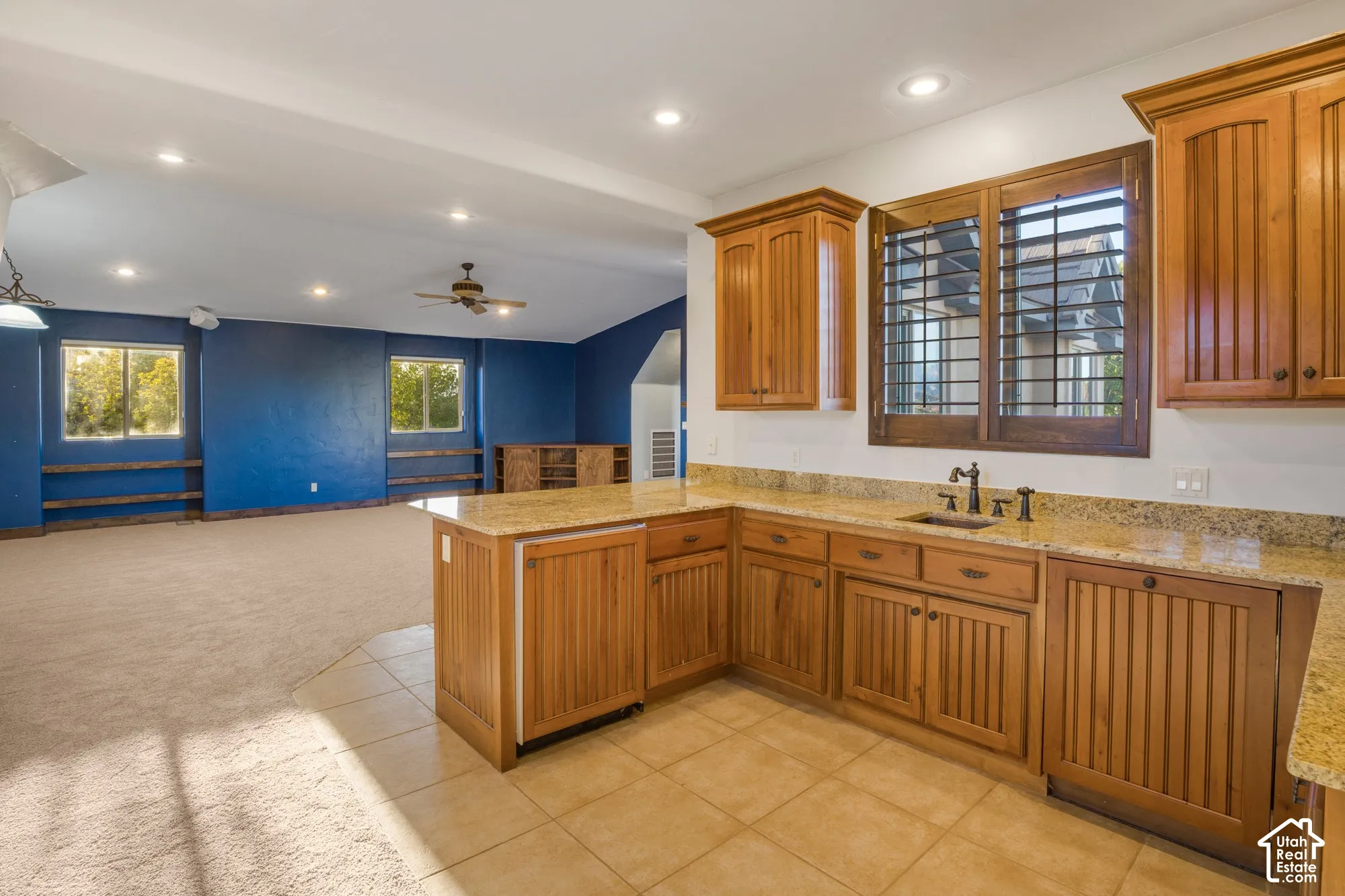 Custom cabinetry with beadboard detailing, stone-surface countertops, recessed ceiling lighting, plantation shutters, and tile flooring