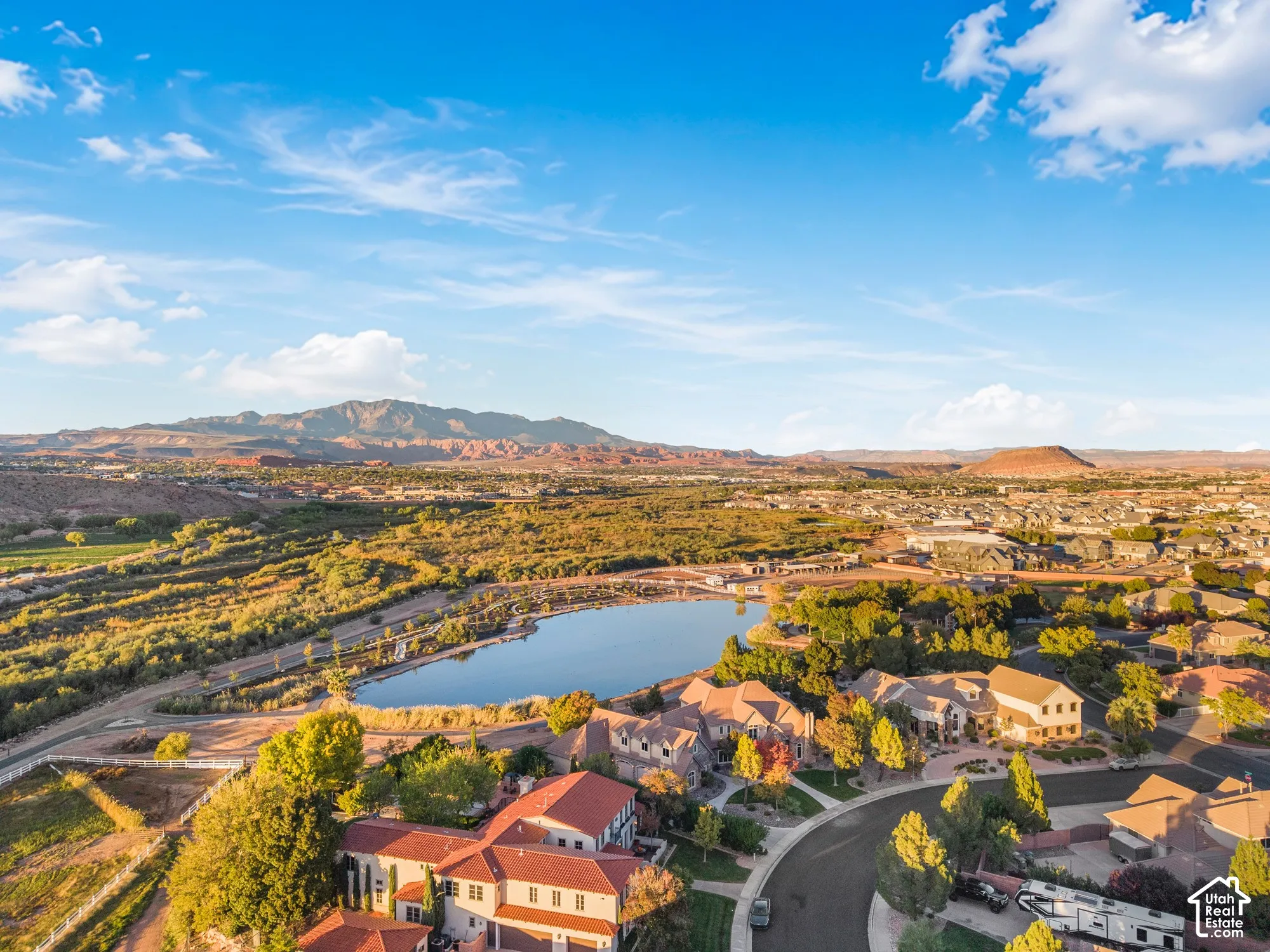 Aerial perspective featuring multi-level residences with red-tile roofs, proximity to a central pond, and a backdrop of expansive mountain ranges