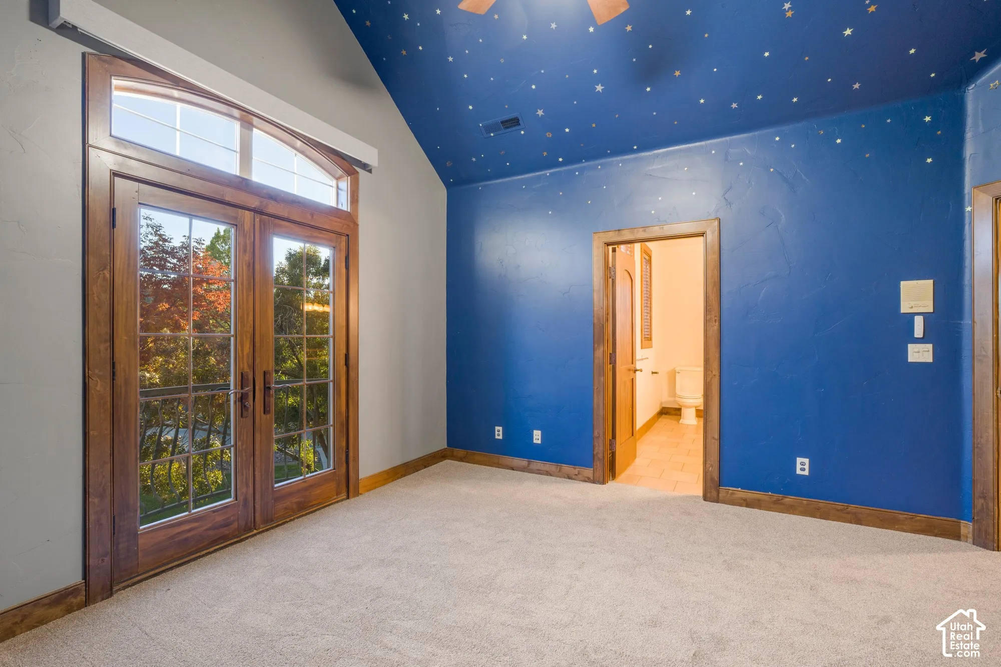 Vaulted ceiling, double French doors with arched transom window, wood-finish trim, and neutral wall-to-wall carpeting