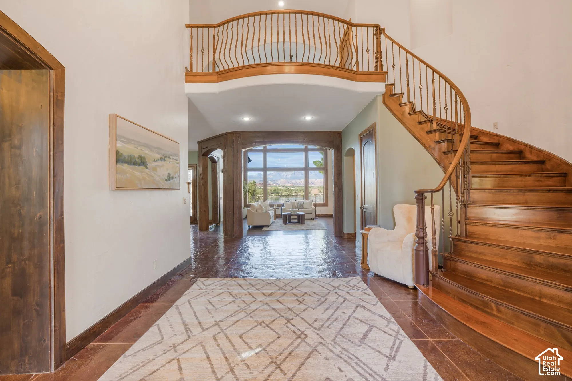Grand foyer featuring a curved wood staircase, decorative metal balusters, polished tile flooring, and an elevated mezzanine walkway