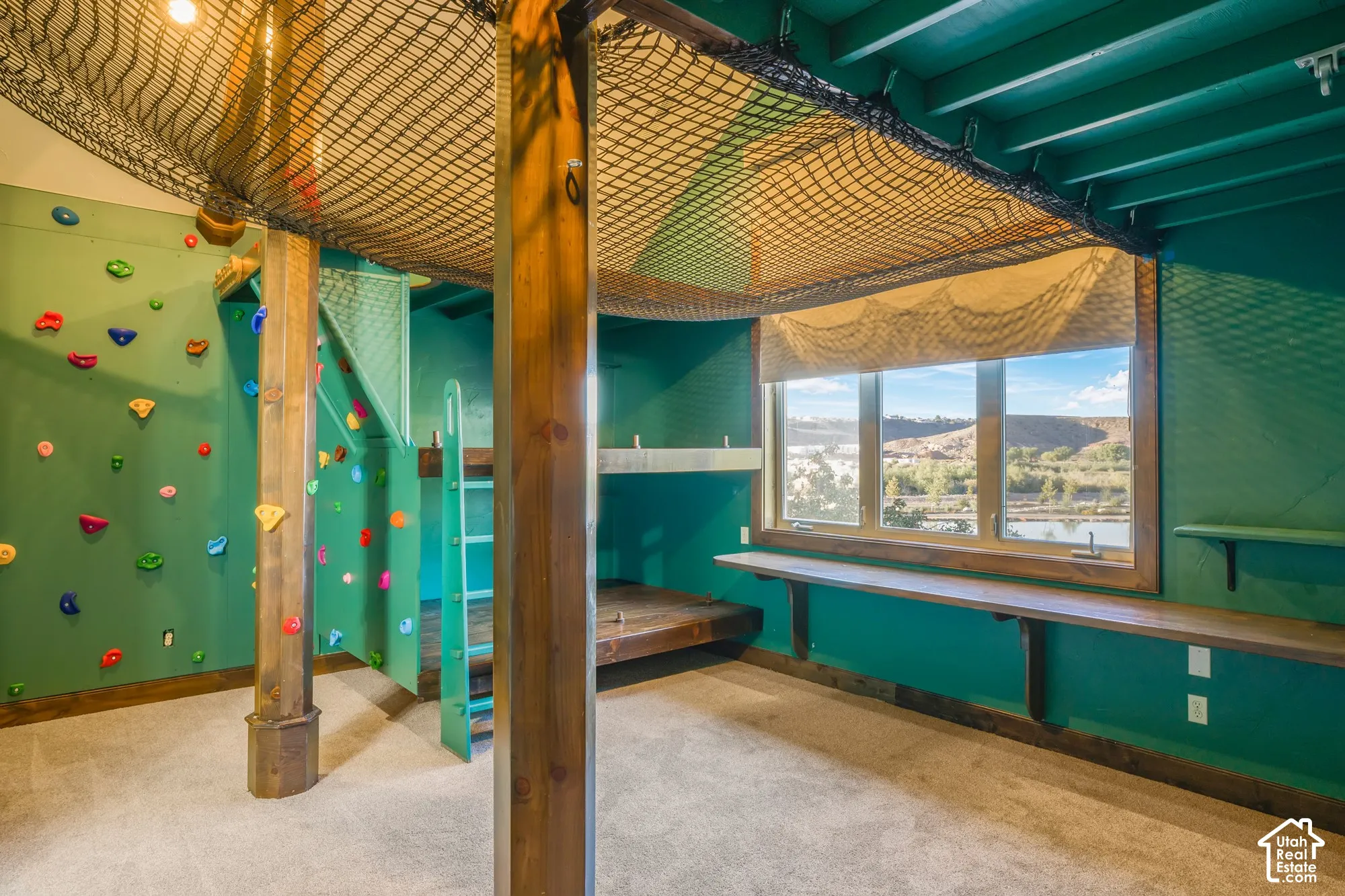 Indoor climbing wall with mounted grips, elevated cargo net feature, built-in wooden sleeping platforms, and a wall-mounted desk