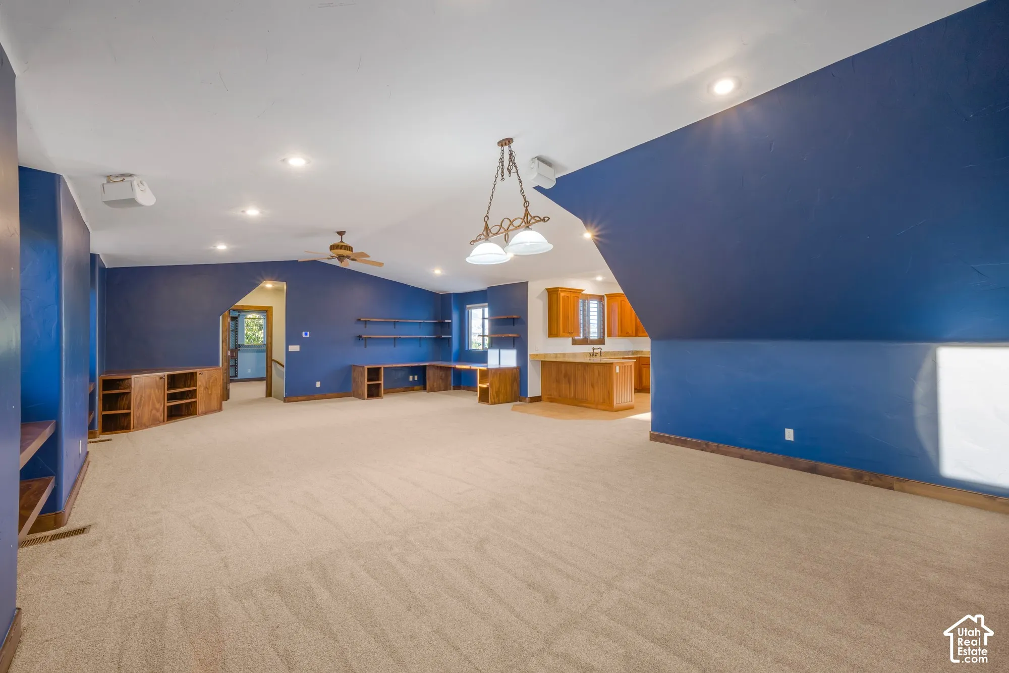 Vaulted ceilings with recessed lighting, built-in wooden cabinetry, integrated desk space, wall-mounted shelving, and kitchenette featuring wooden cabinetry